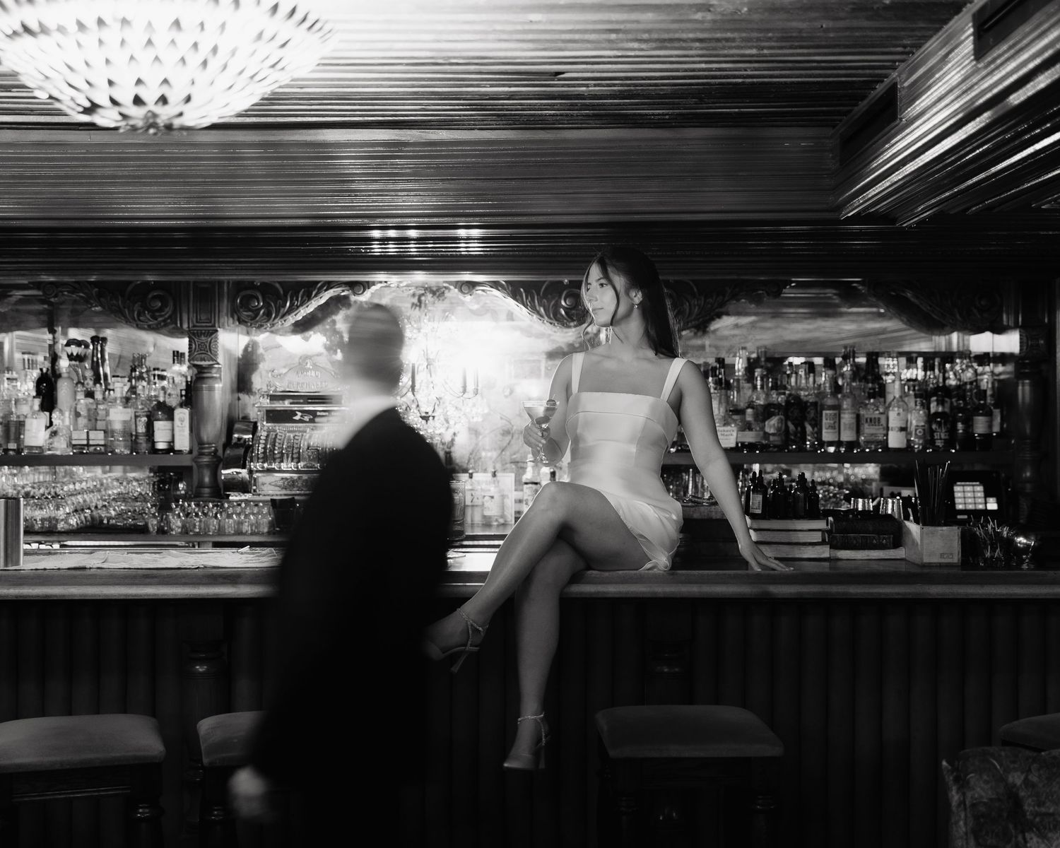 Vintage bar scene showing silhouetted figures in a dimly lit lounge with bottles and glassware on display.