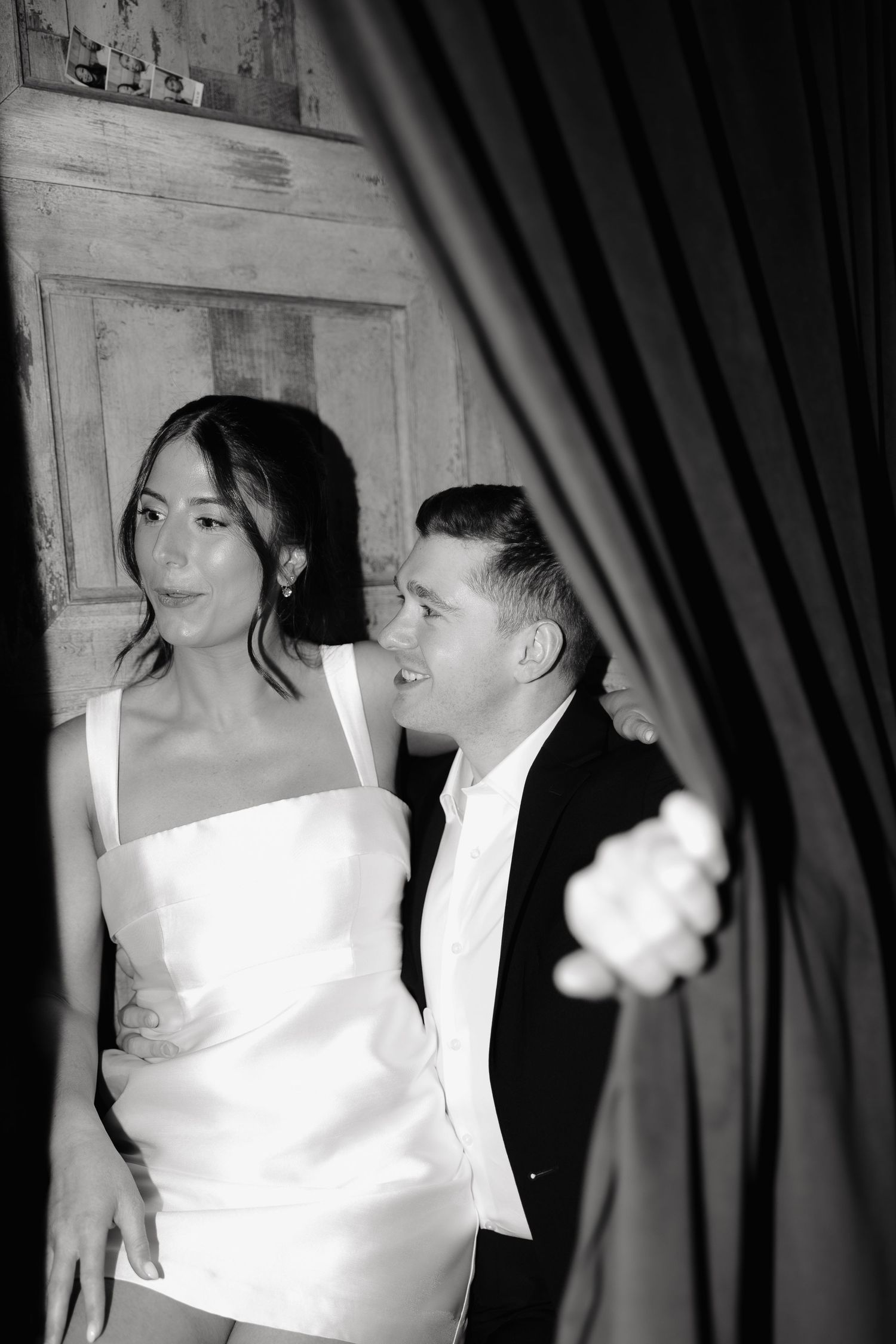 A black and white photo of a couple at a formal event, with the woman in a white dress and man in a tuxedo.