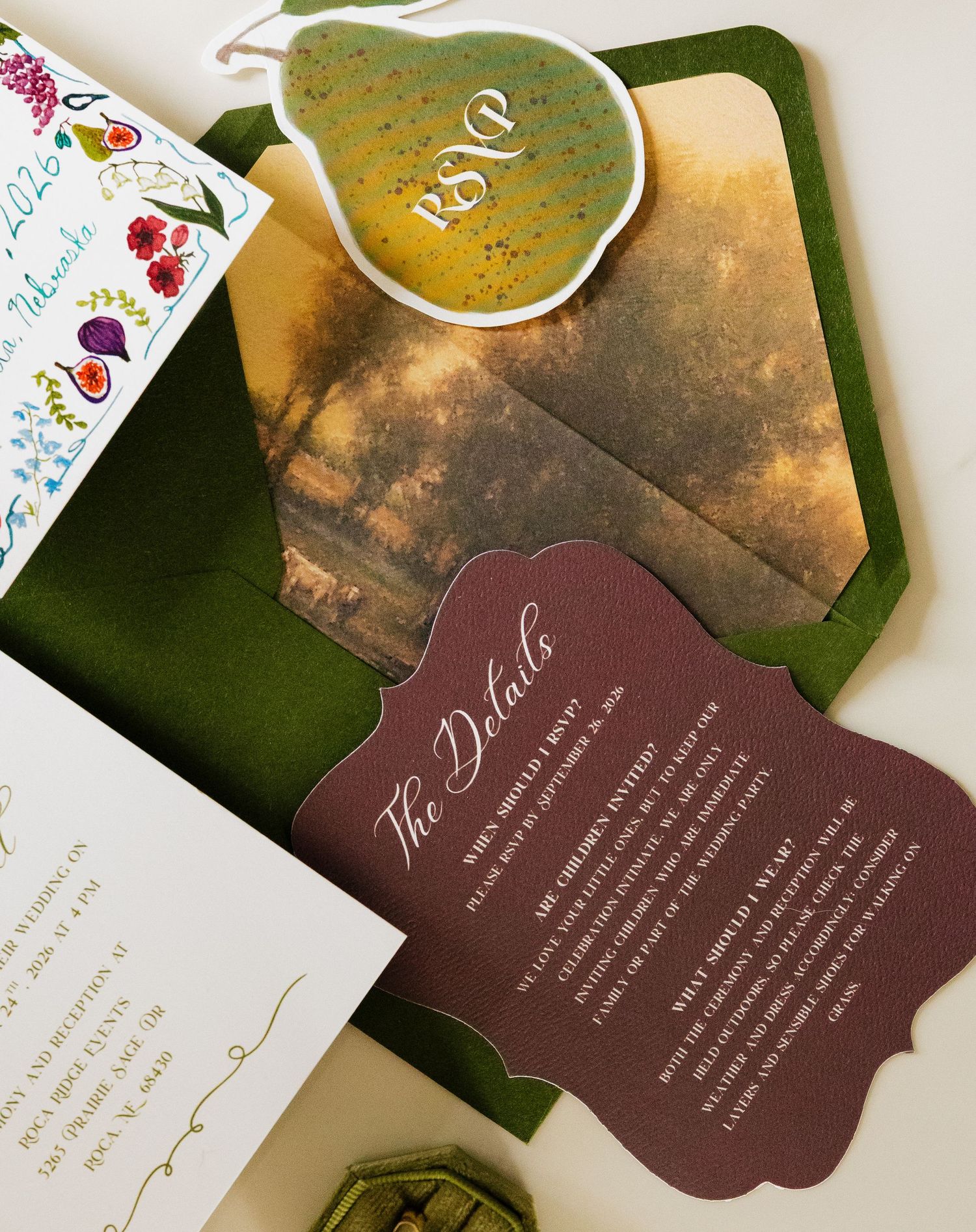 Wedding invitation suite with a green pear-shaped tag, olive envelope liner, burgundy scalloped details card, and floral watercolor accents.