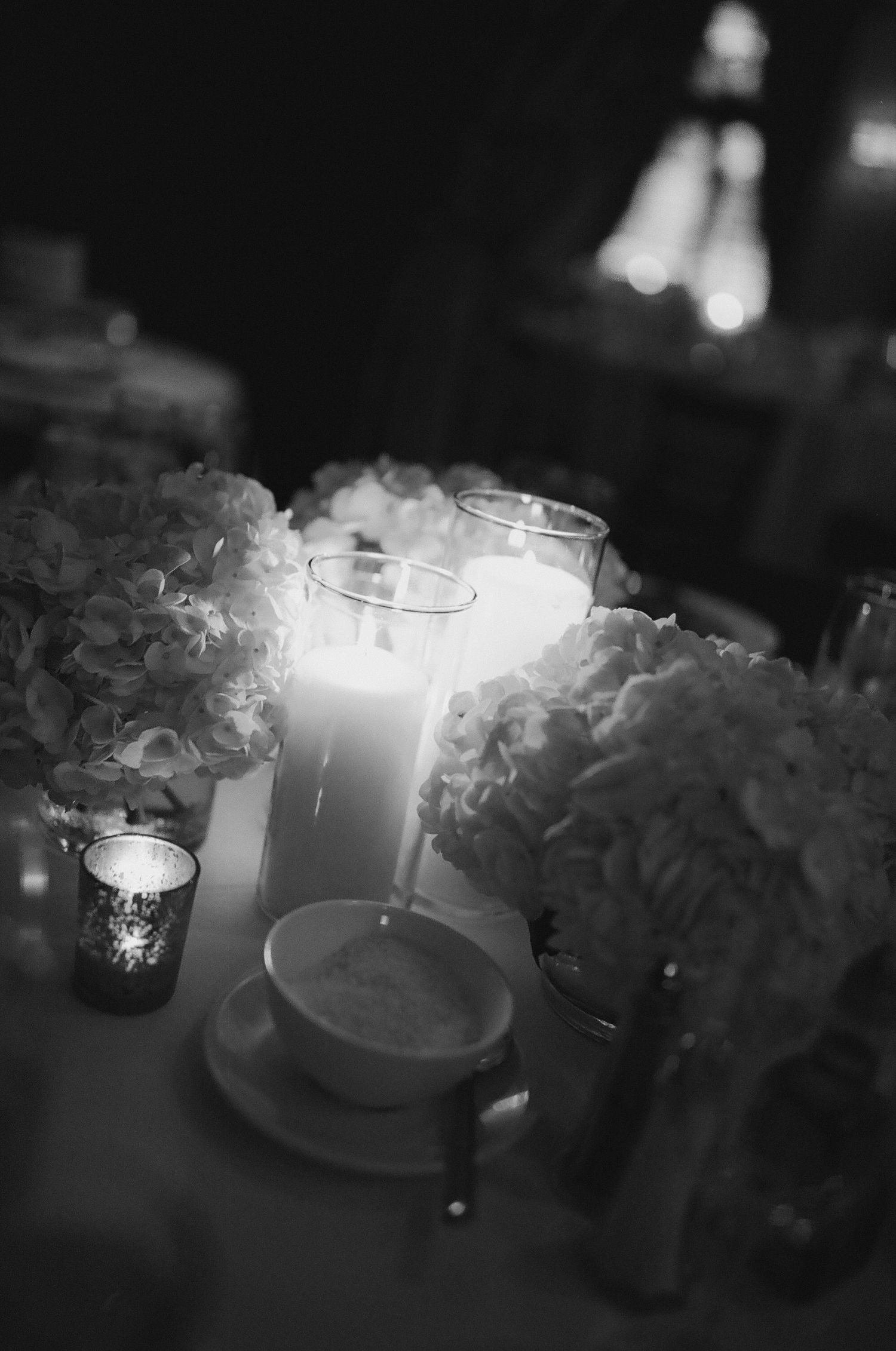 Black and white photo of elegant wedding table centerpiece with white hydrangeas and tall pillar candle.