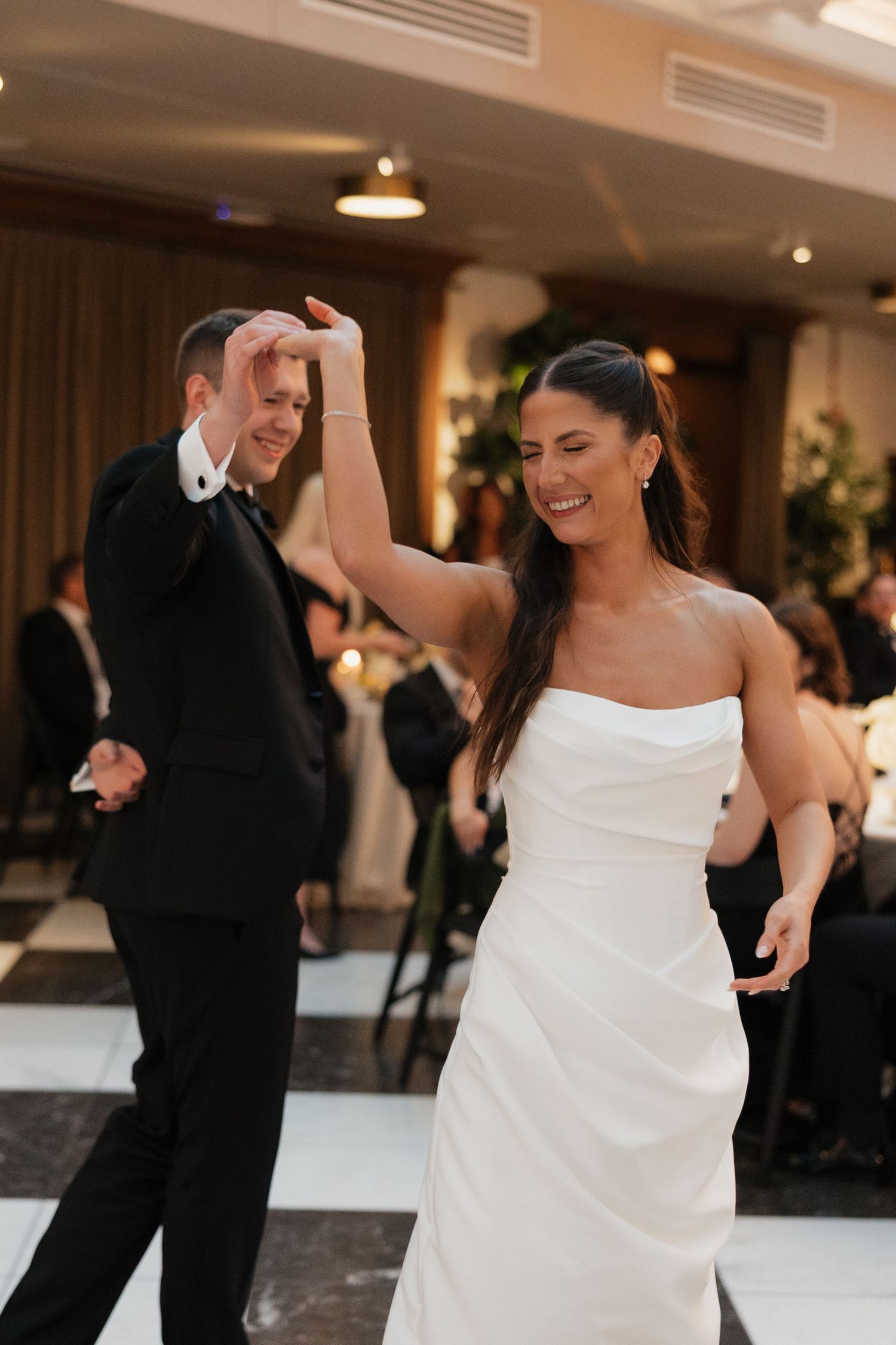 Bride and groom share their first dance, smiling joyfully on a checkered dance floor at their elegant wedding reception.