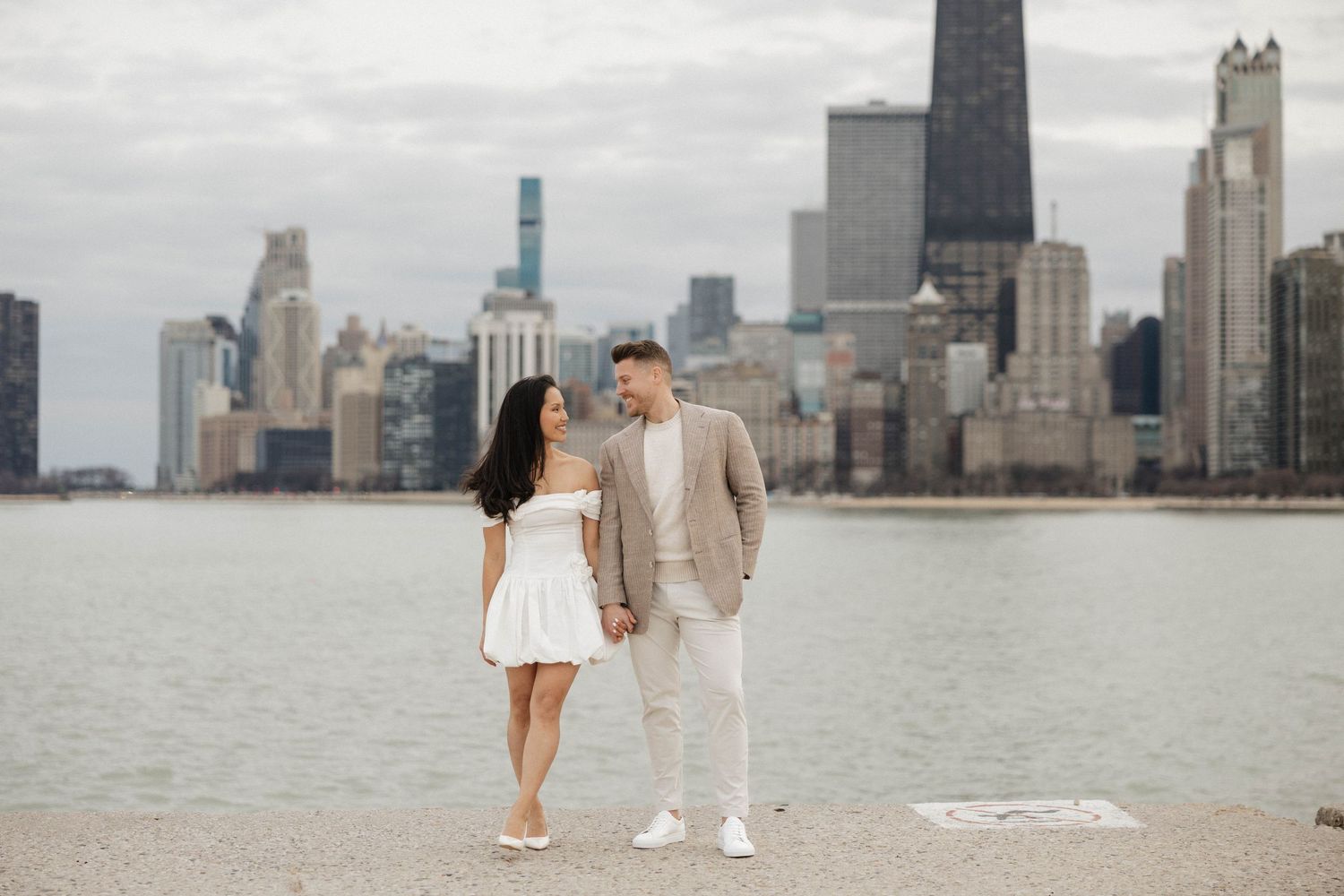 Couple holding hands smiling at each other with Chicago skyline and lake in background.