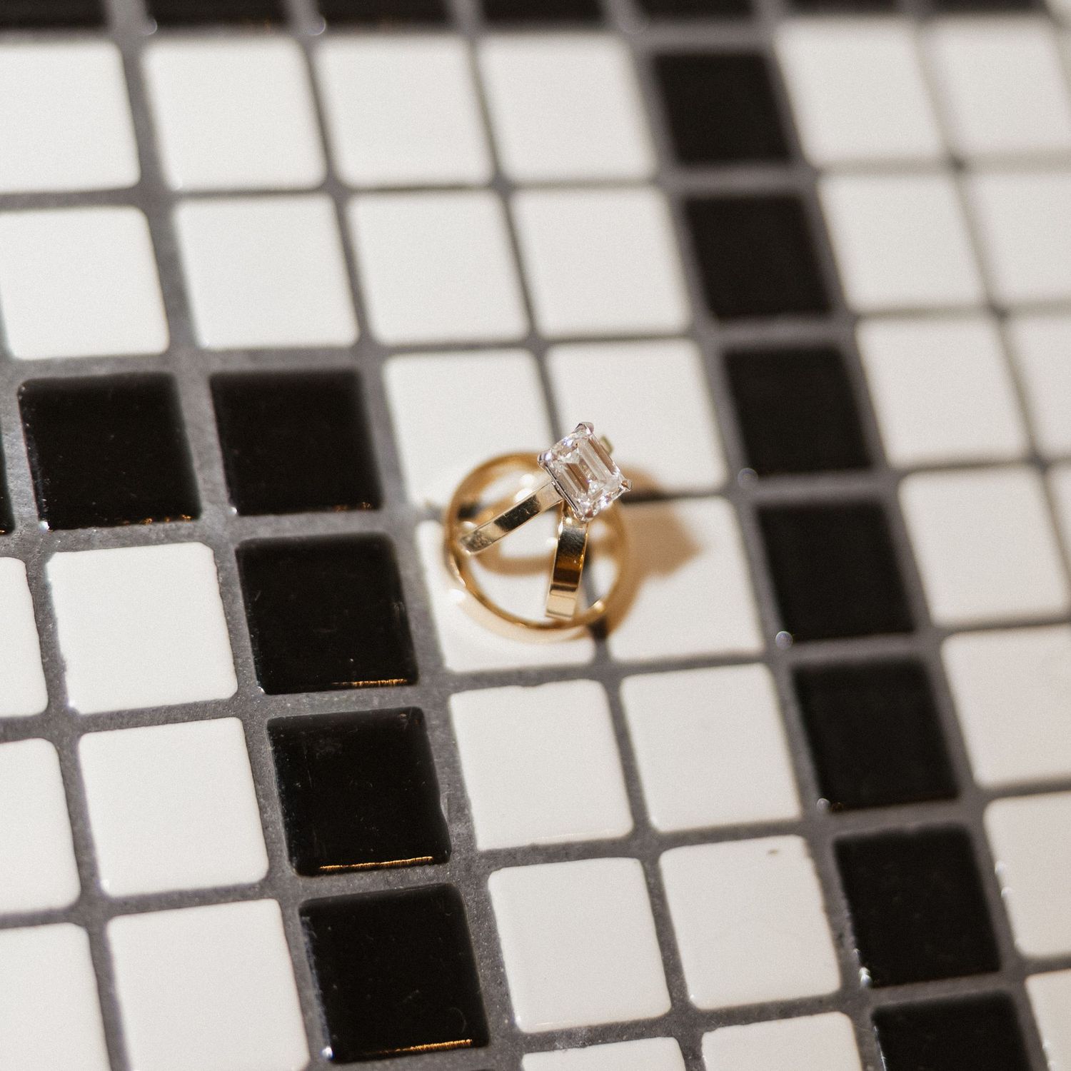Gold wedding rings displayed on a white and black tiled mosaic surface with selective focus.