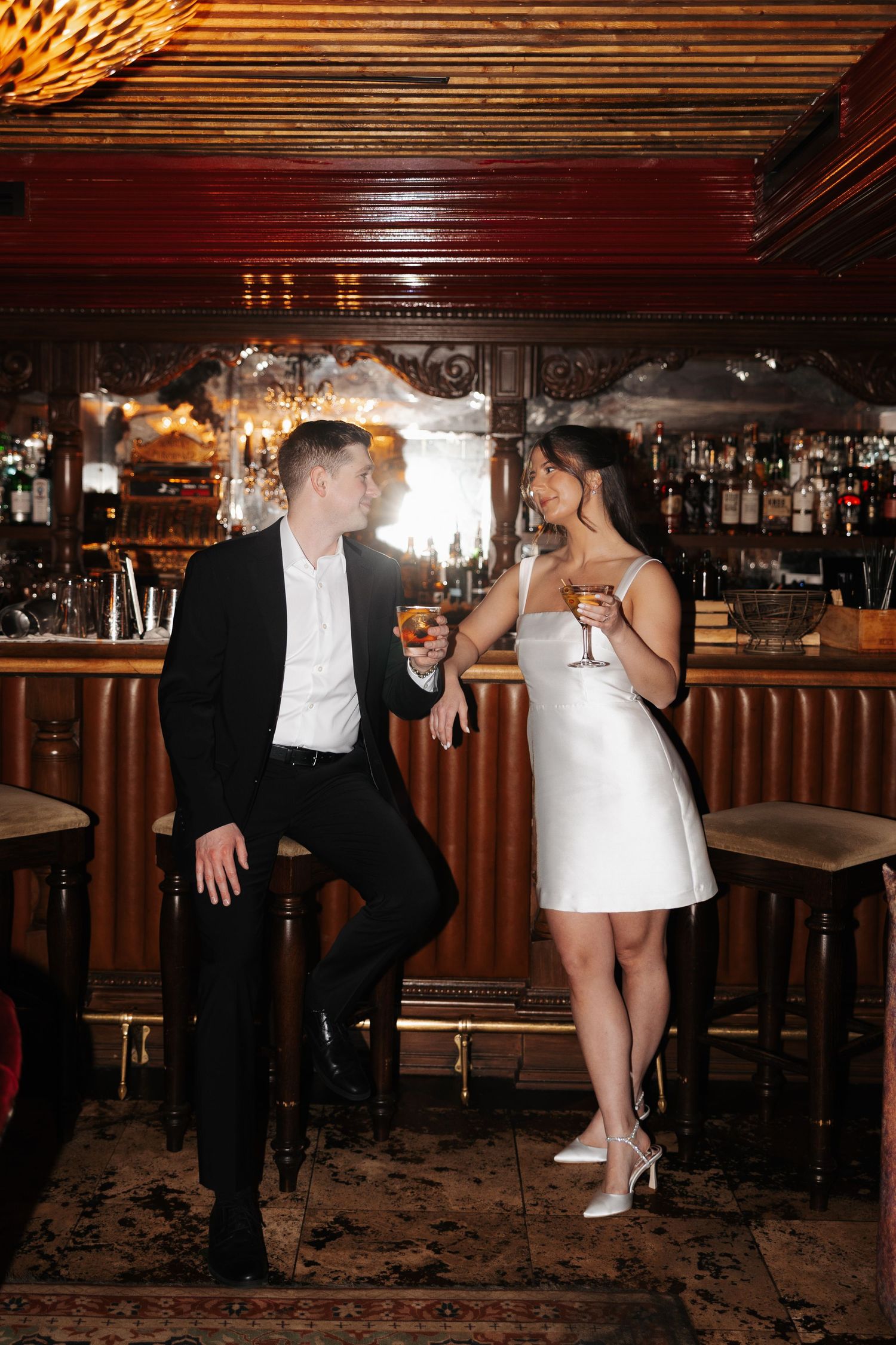 A couple shares a playful moment at a bar with wooden decor and warm lighting.