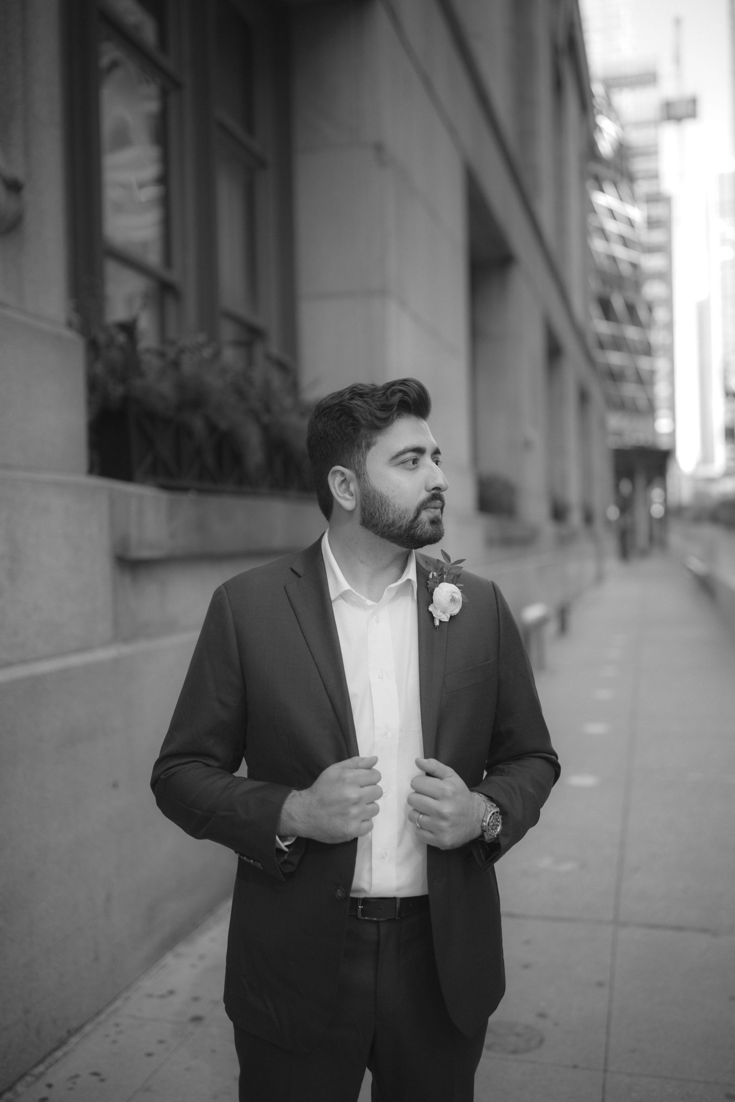 Black and white portrait series of a groom in a formal suit adjusting his jacket on a city street.