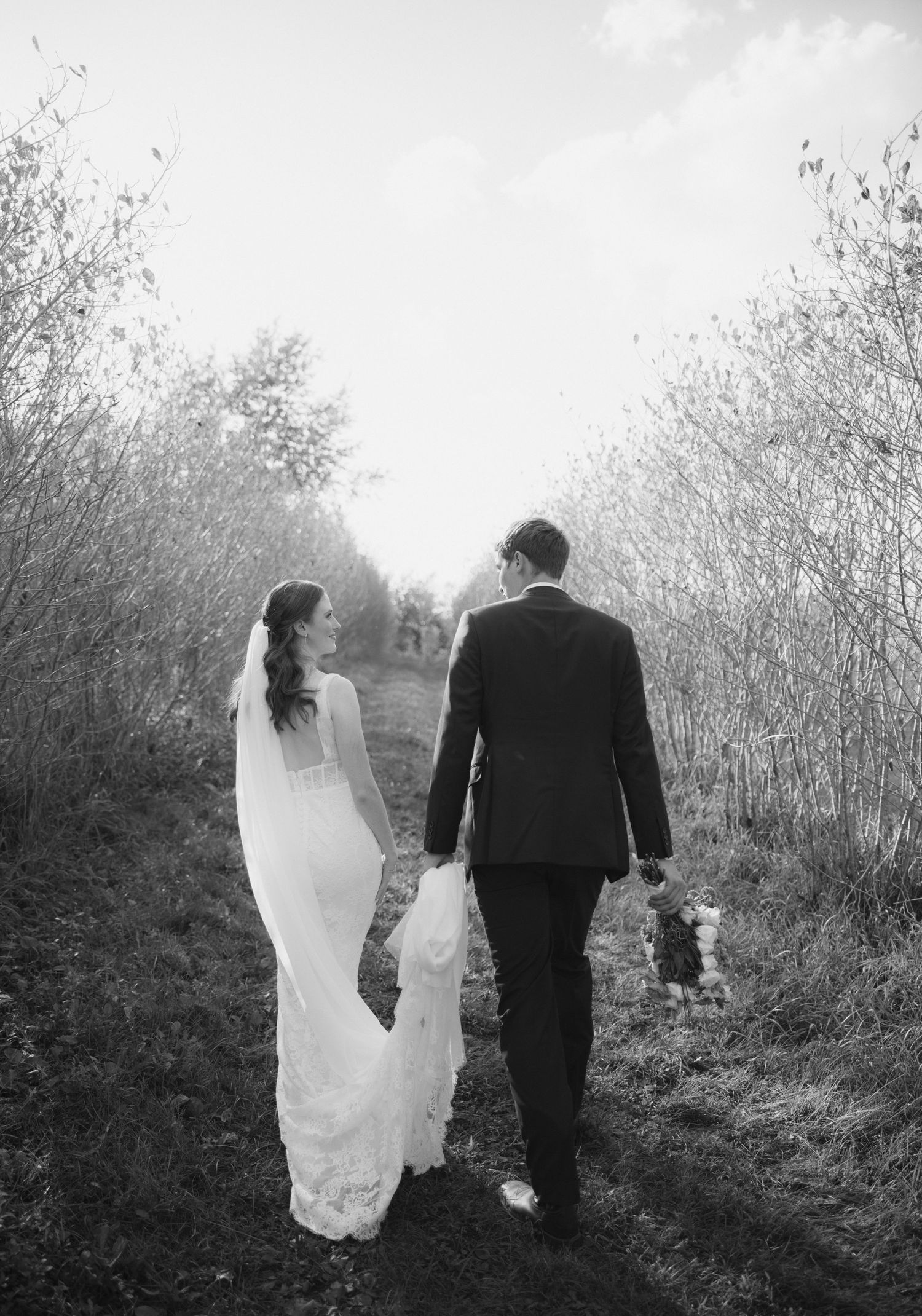 Black and white photo of a couple walking down a misty path in wedding attire.