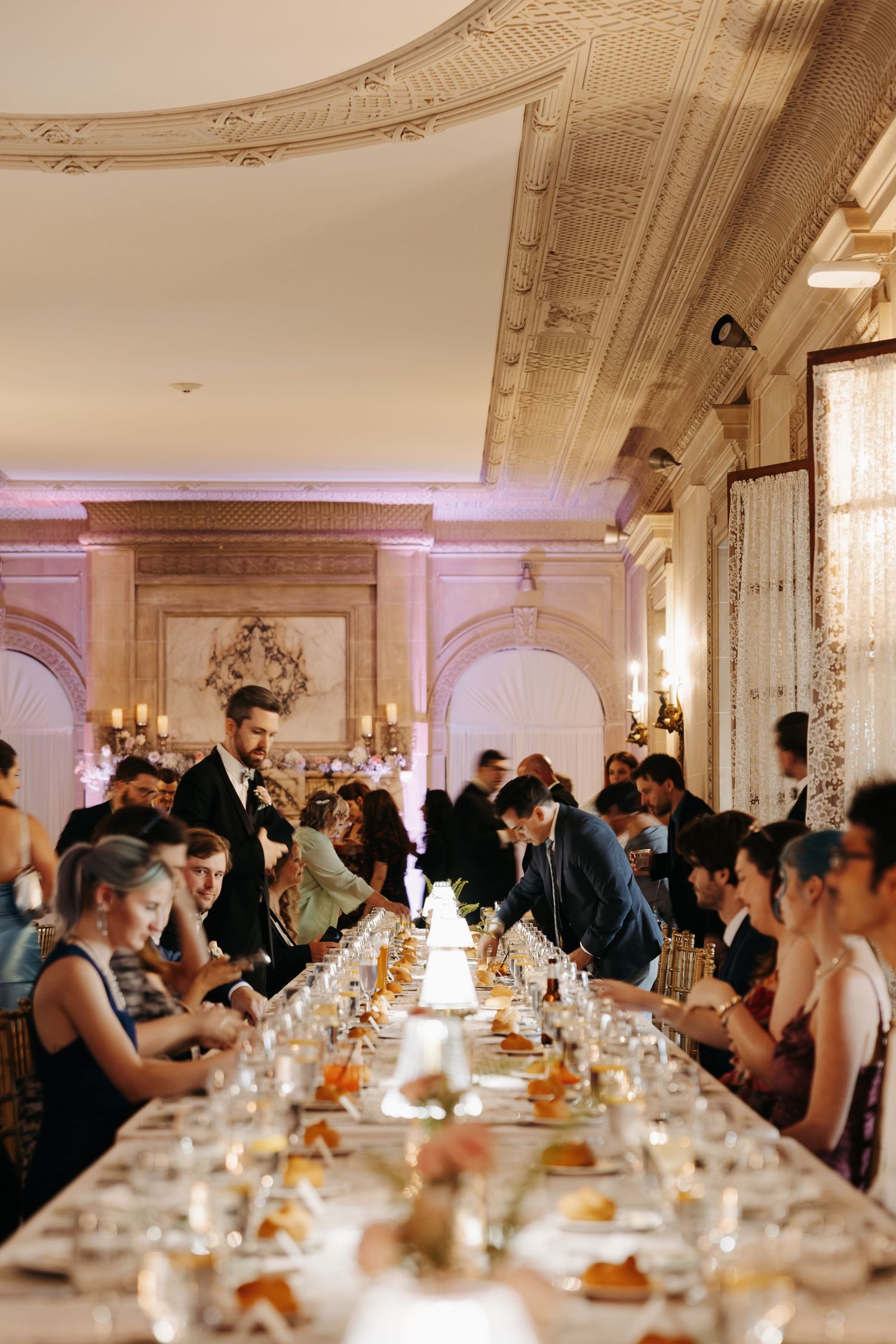Elegant wedding reception in a grand ballroom with long dining tables, ornate ceiling, and warm candlelight ambiance.