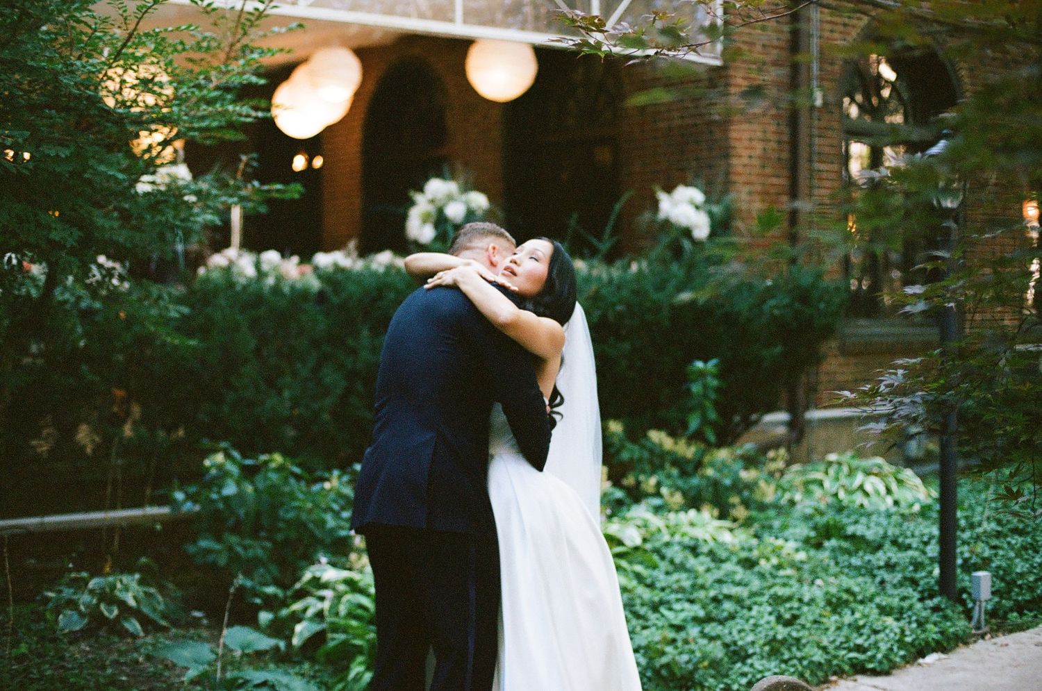 Bride and groom share a romantic embrace in a lush garden courtyard during their wedding day.