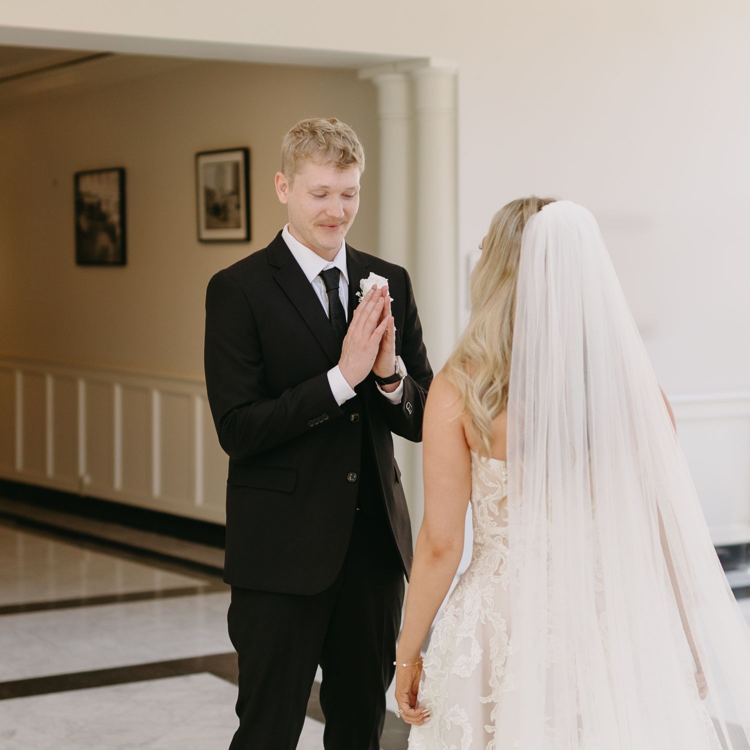 Emotional first look wedding moment captured in a bright hallway as the couple shares a touching reaction.