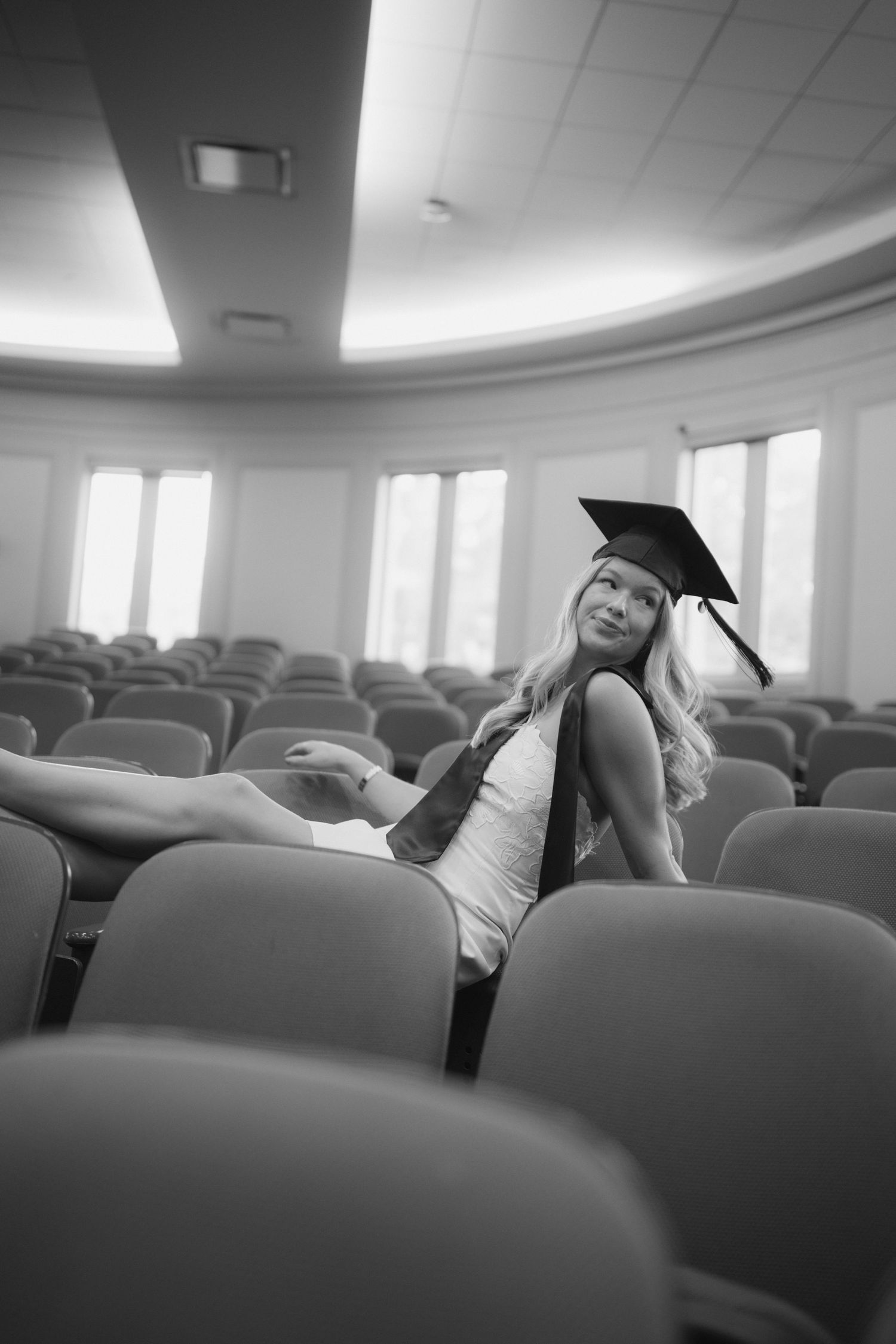 Black and white photo series showing a person sitting and laughing in an empty auditorium with rows of chairs.