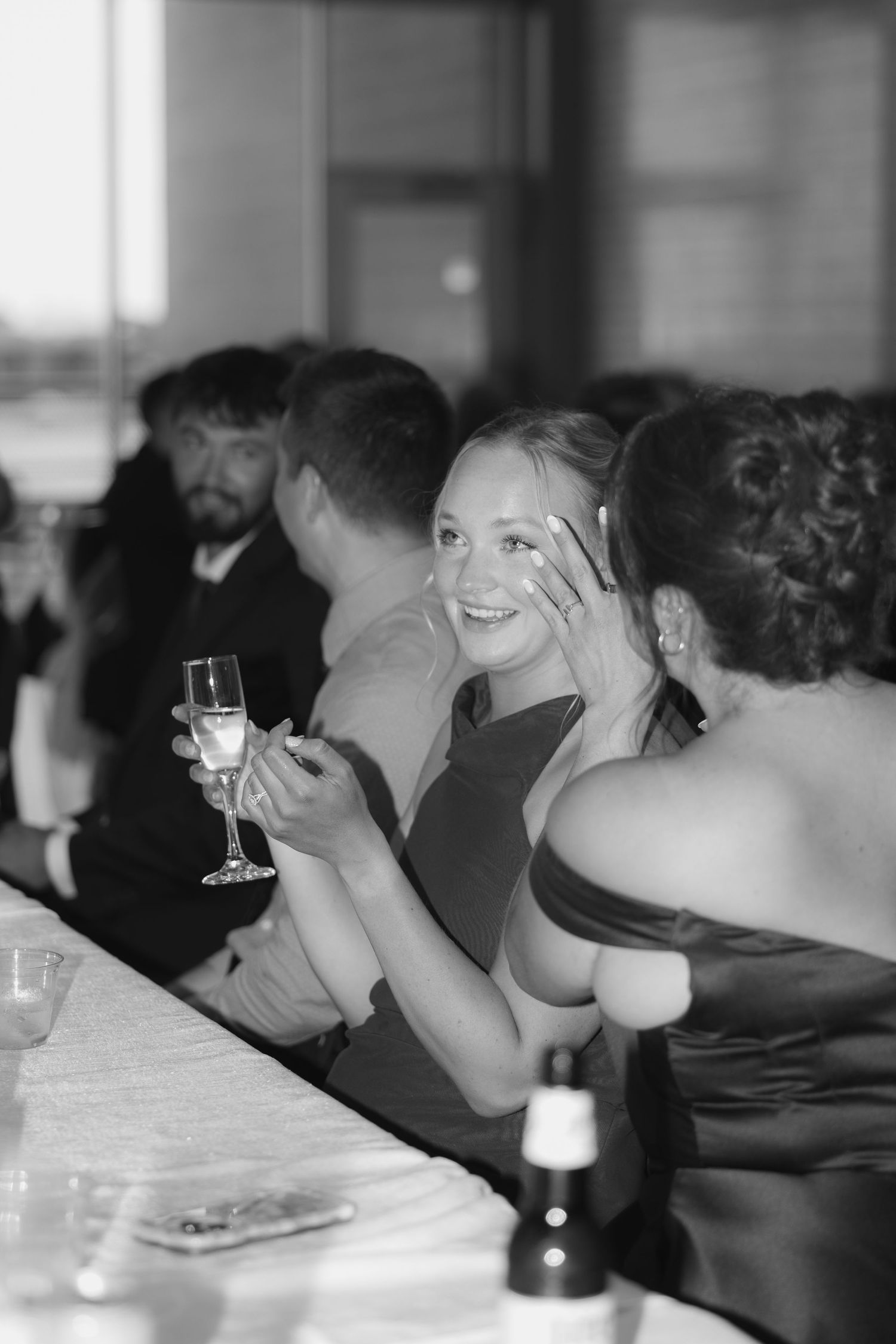 Black and white photo of a smiling woman holding champagne glass at a formal event.