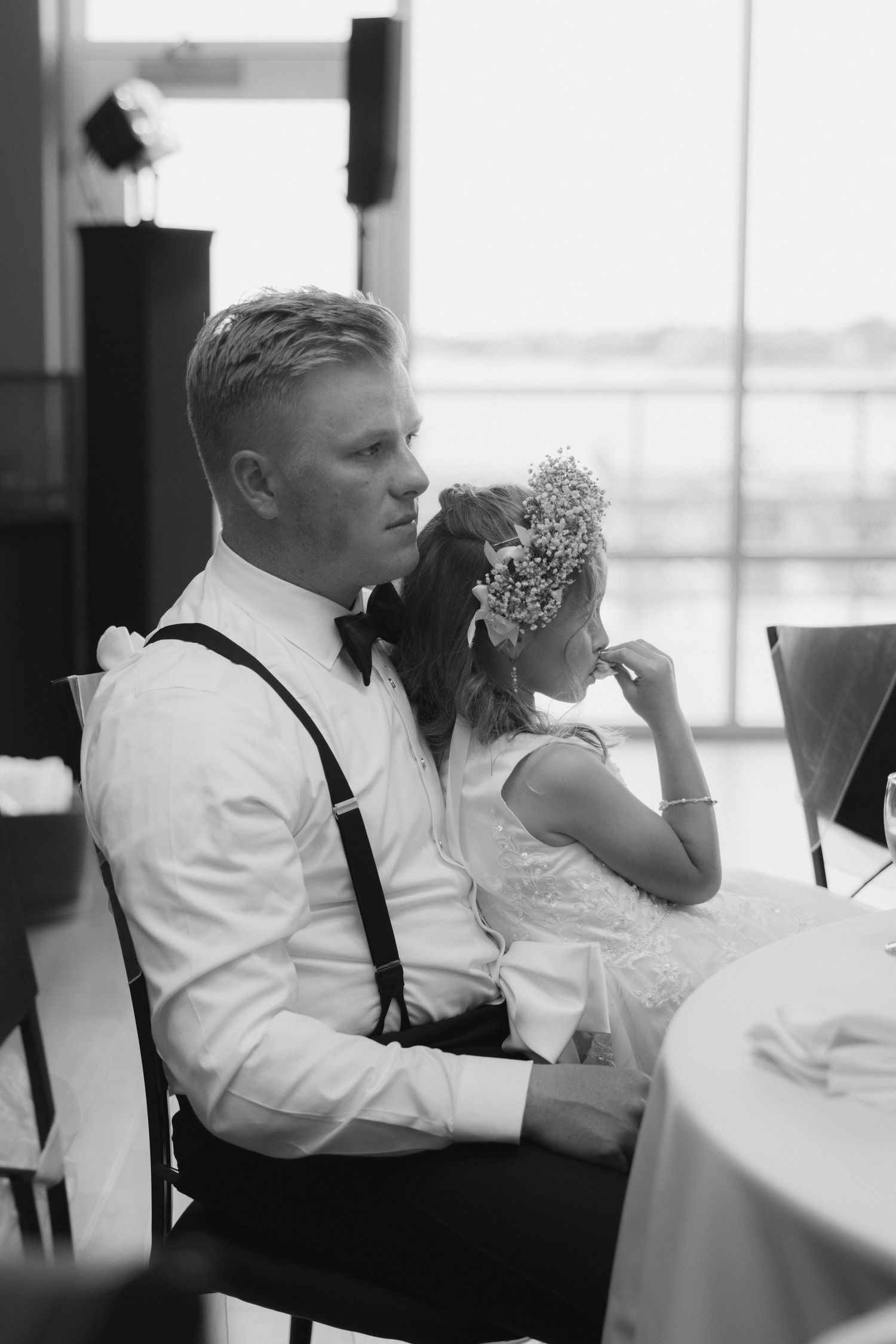 Black and white photo of a bride and groom seated at a wedding reception table, bride holding a floral bouquet.