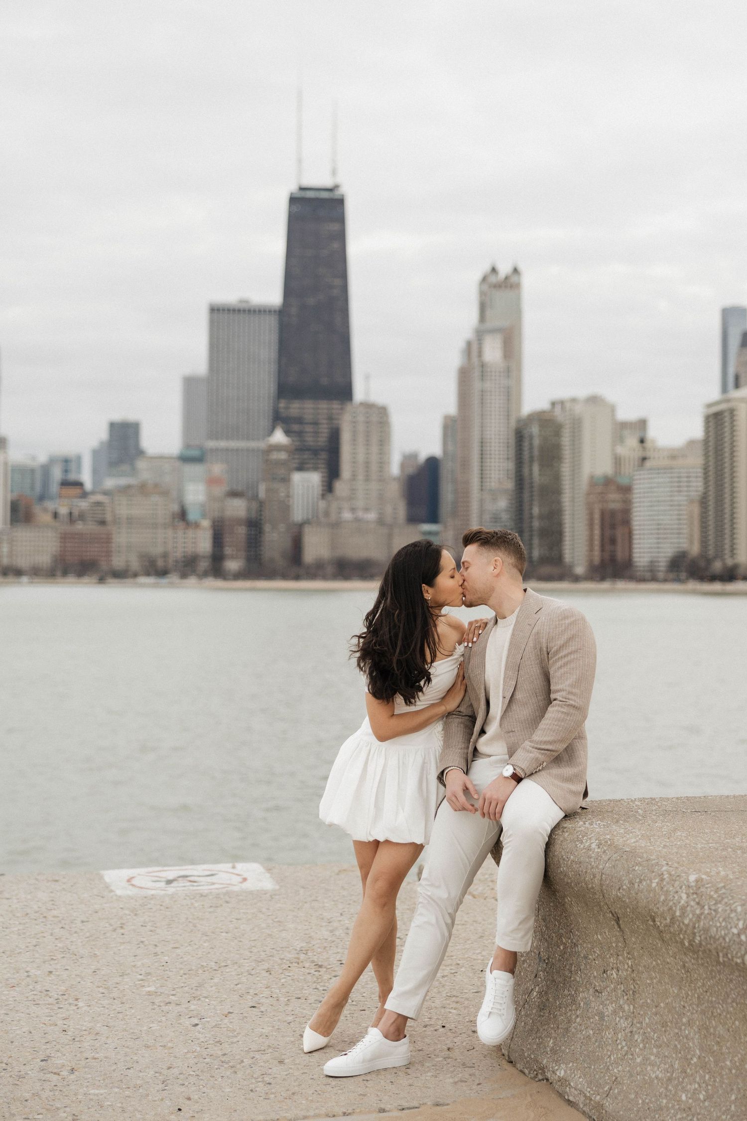Couple sharing a kiss by Lake Michigan with Chicago skyline and John Hancock Center in the background.