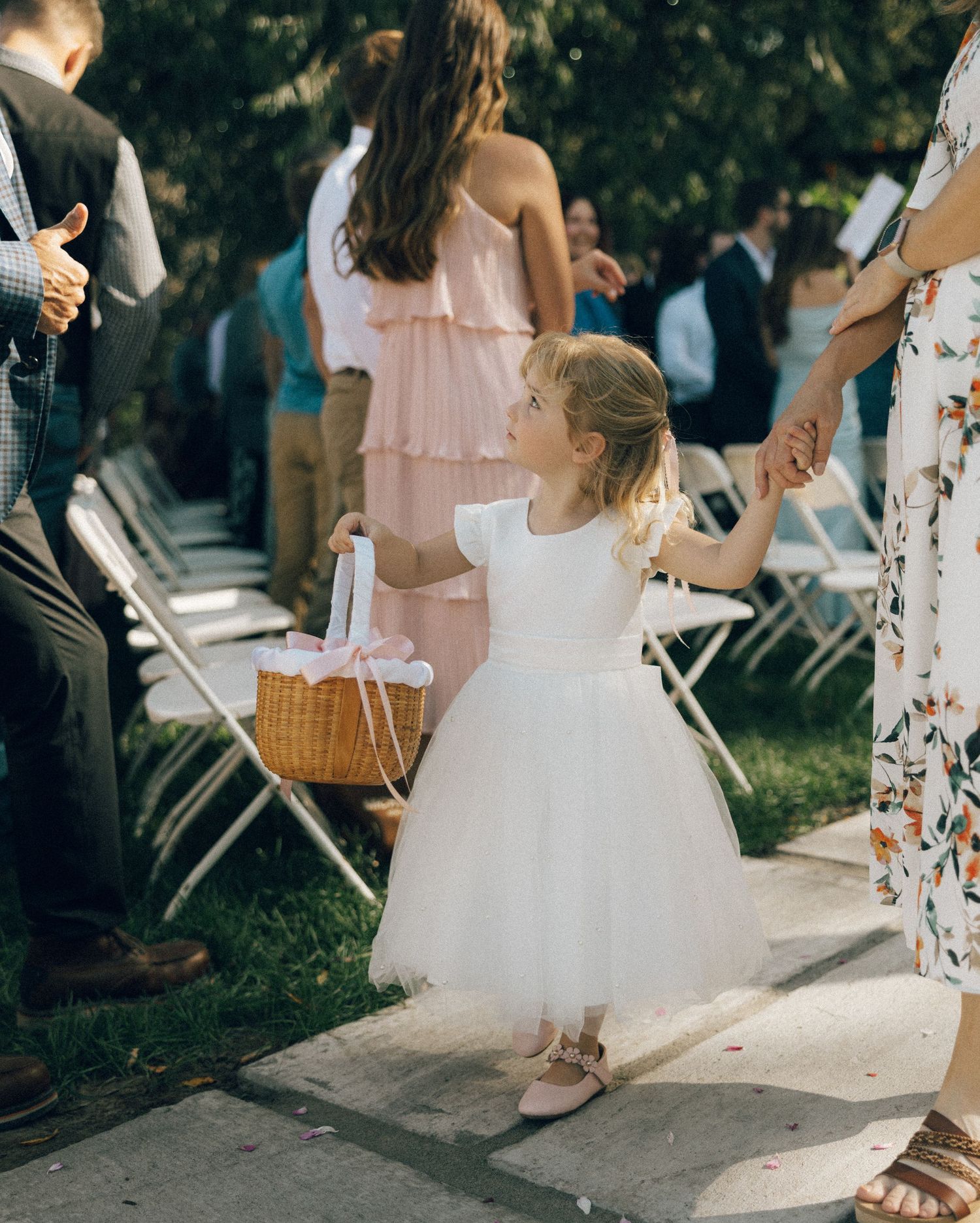 Wedding ceremony details showing flower petals and bridesmaids in pink dresses.