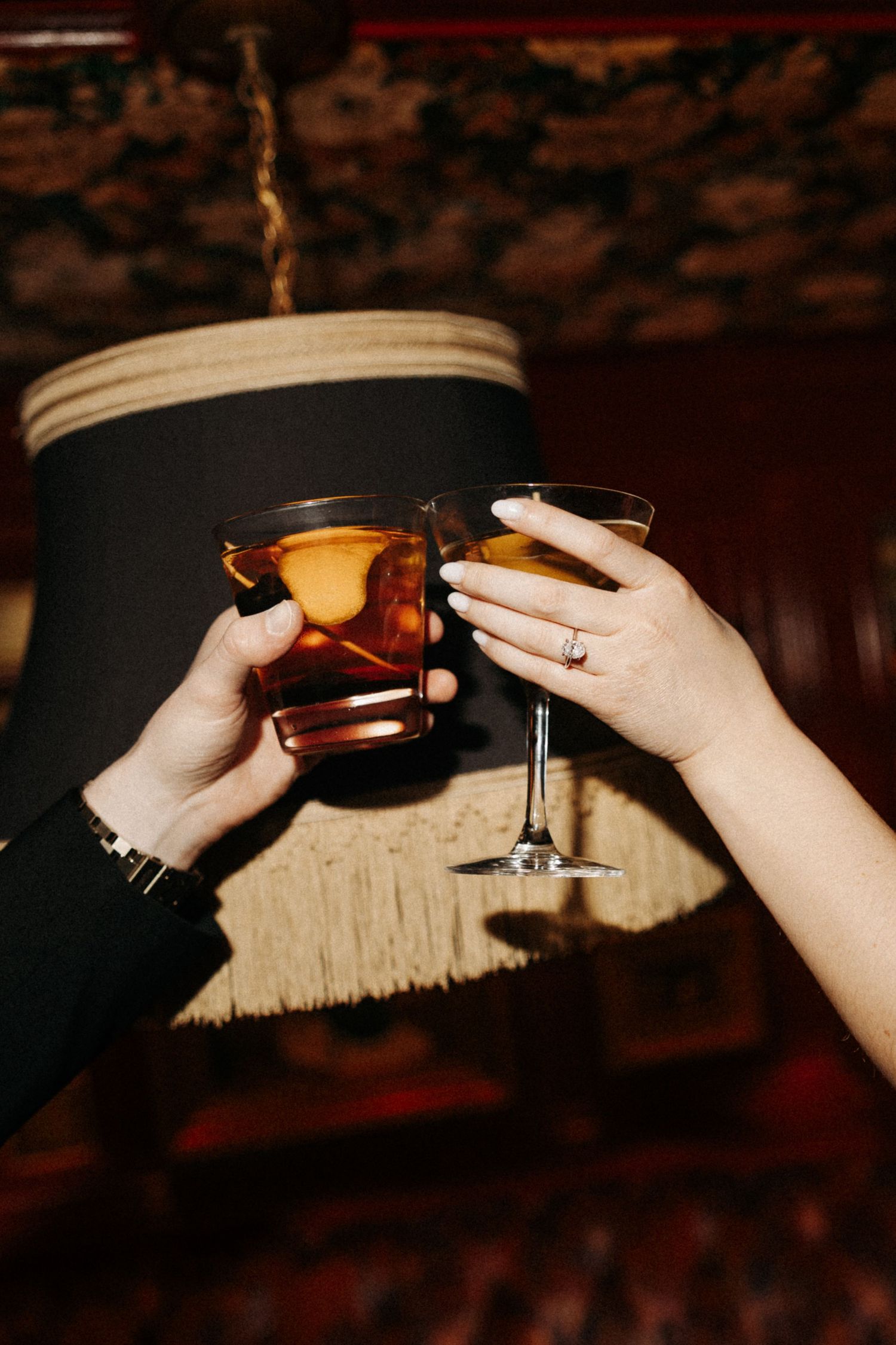 A series of hands holding and toasting with cocktail glasses in a dimly lit bar setting.