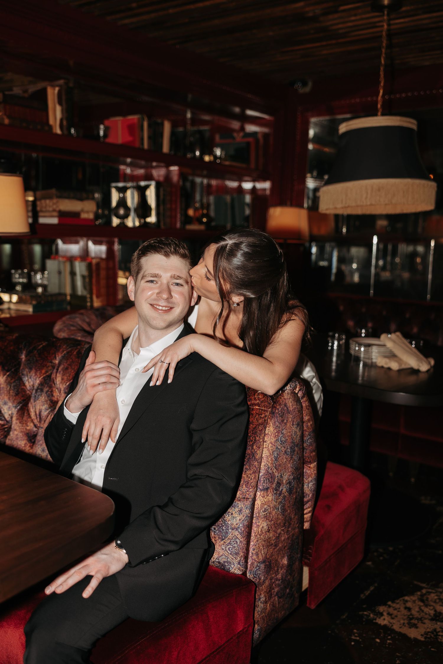 Intimate moment captured between couple on red velvet seating in dark restaurant ambiance.