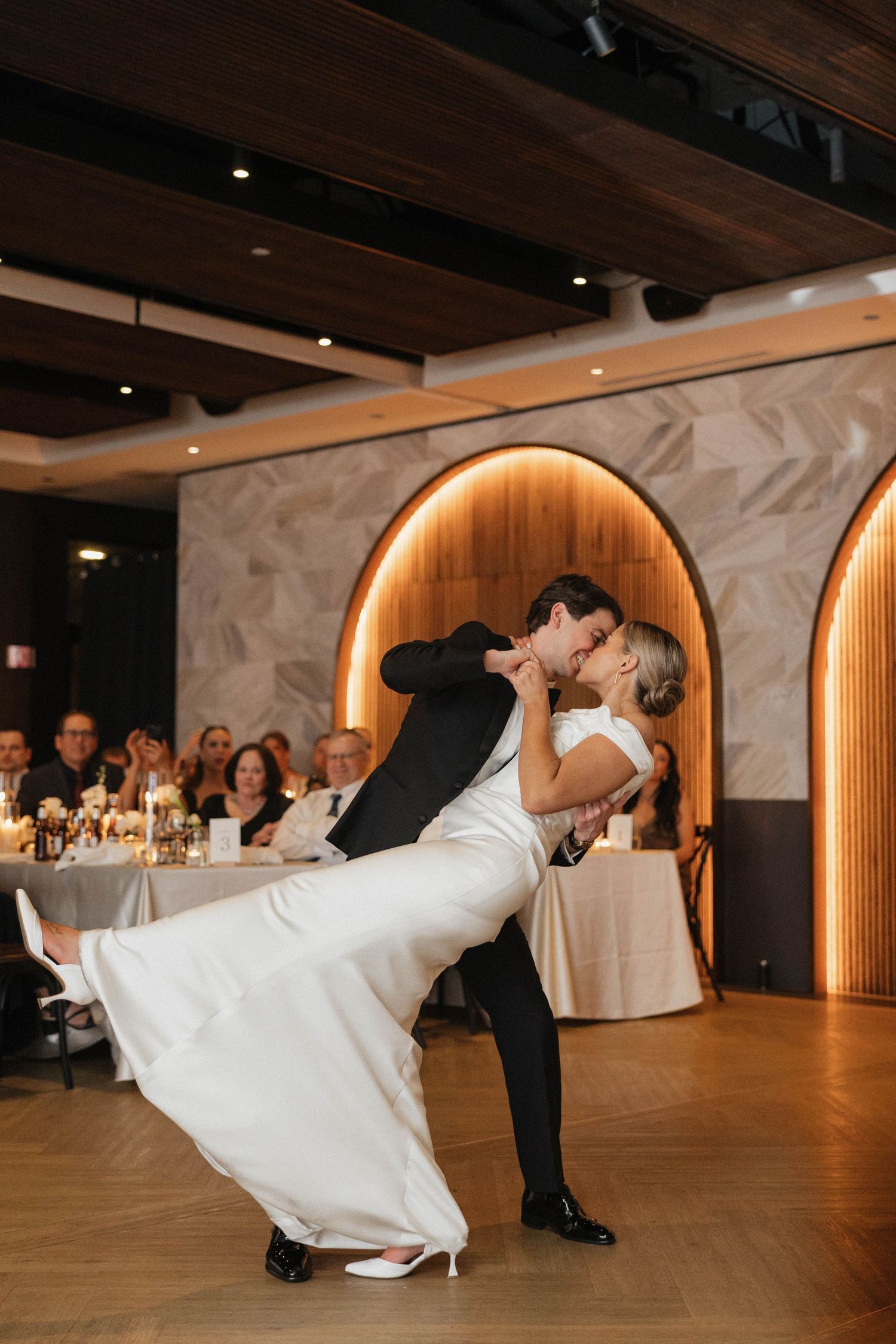 Bride and groom share a romantic dip kiss on the dance floor during their wedding reception.