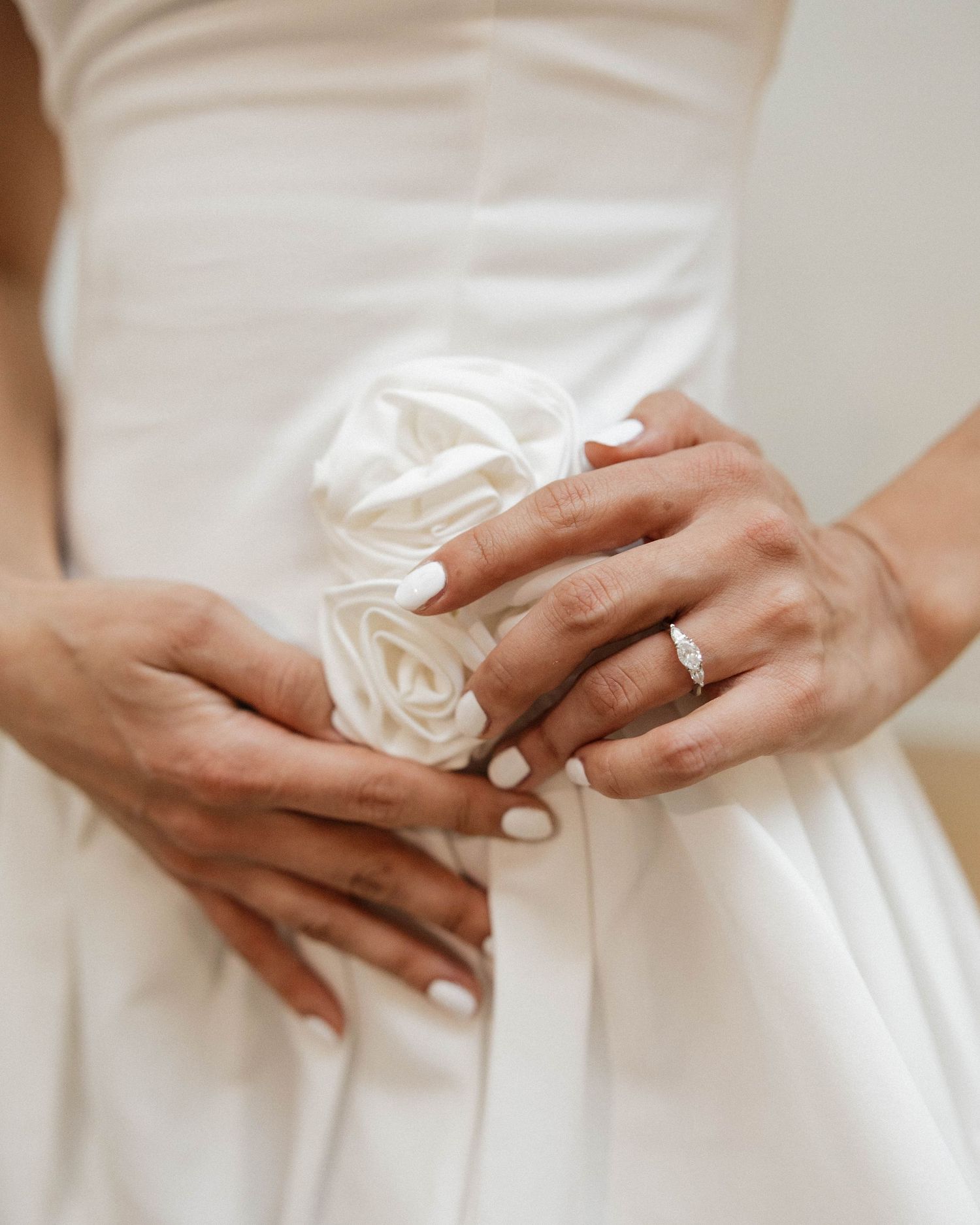 Close-up of bride's hands holding white rose bouquet, wearing diamond engagement ring with white manicure.