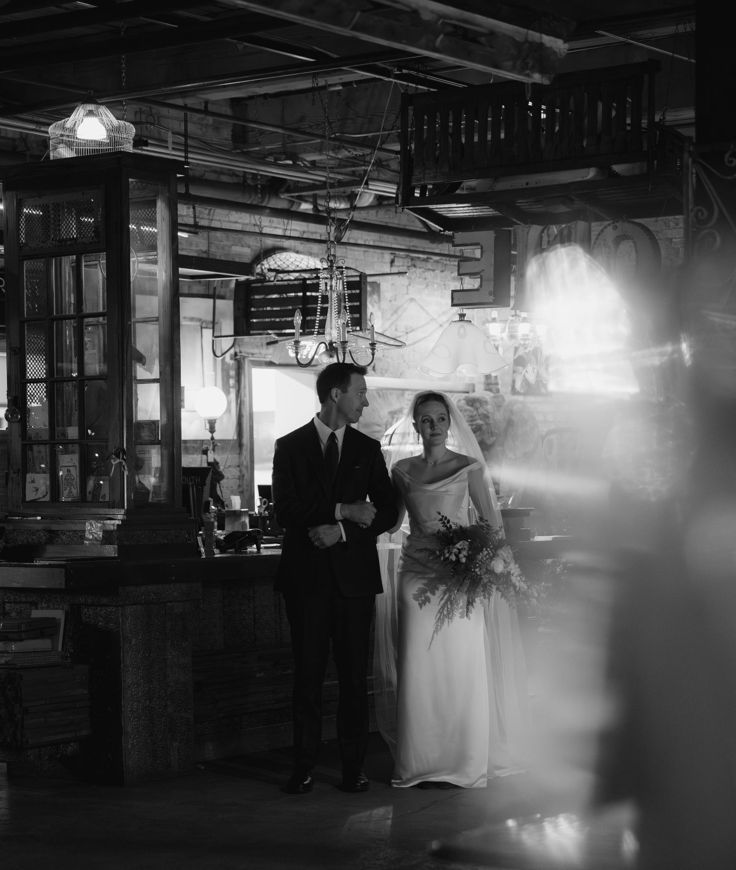 A black and white wedding photograph shows silhouettes of a couple dancing in a dimly lit reception hall.