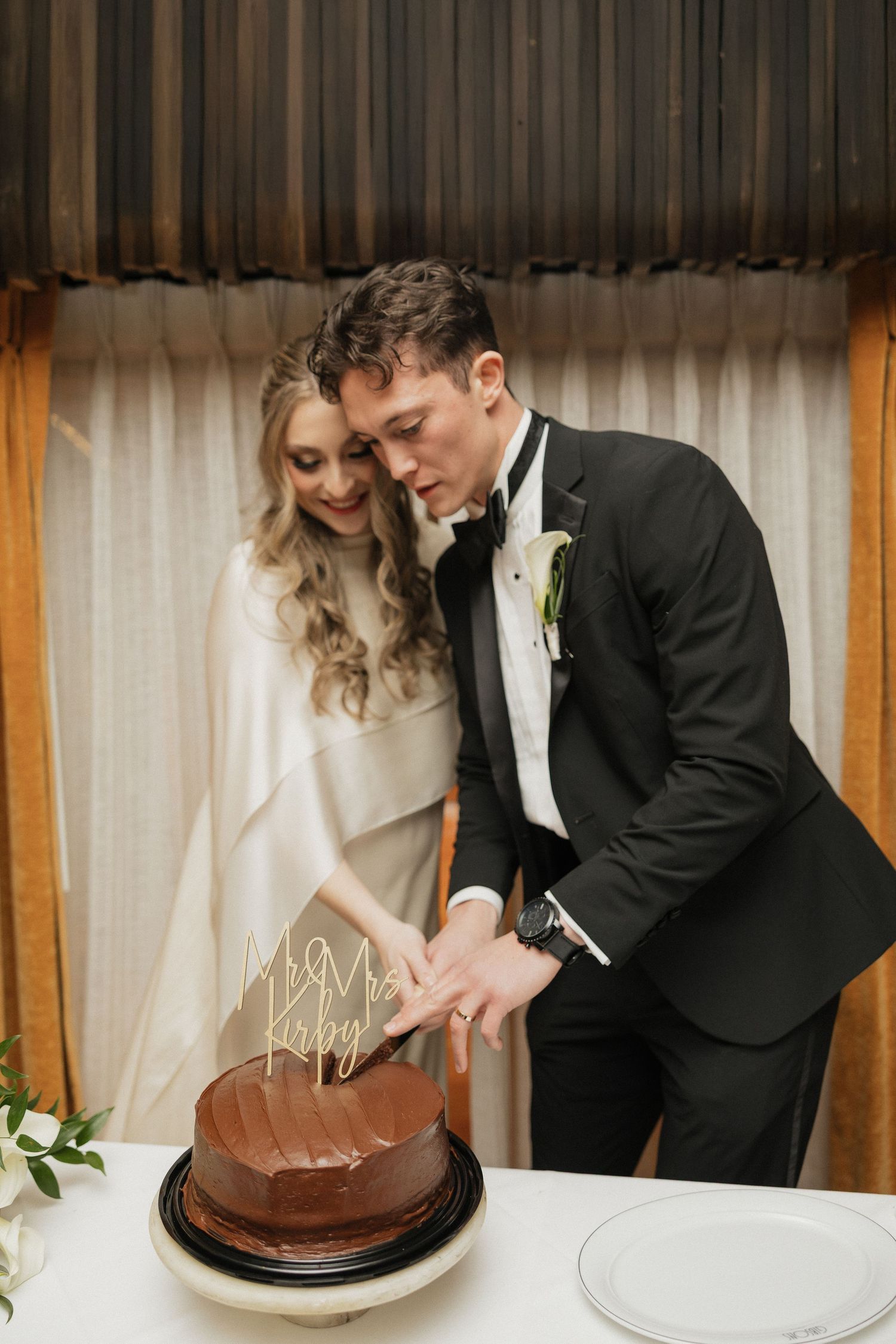 Couple cutting into a chocolate wedding cake together at reception.