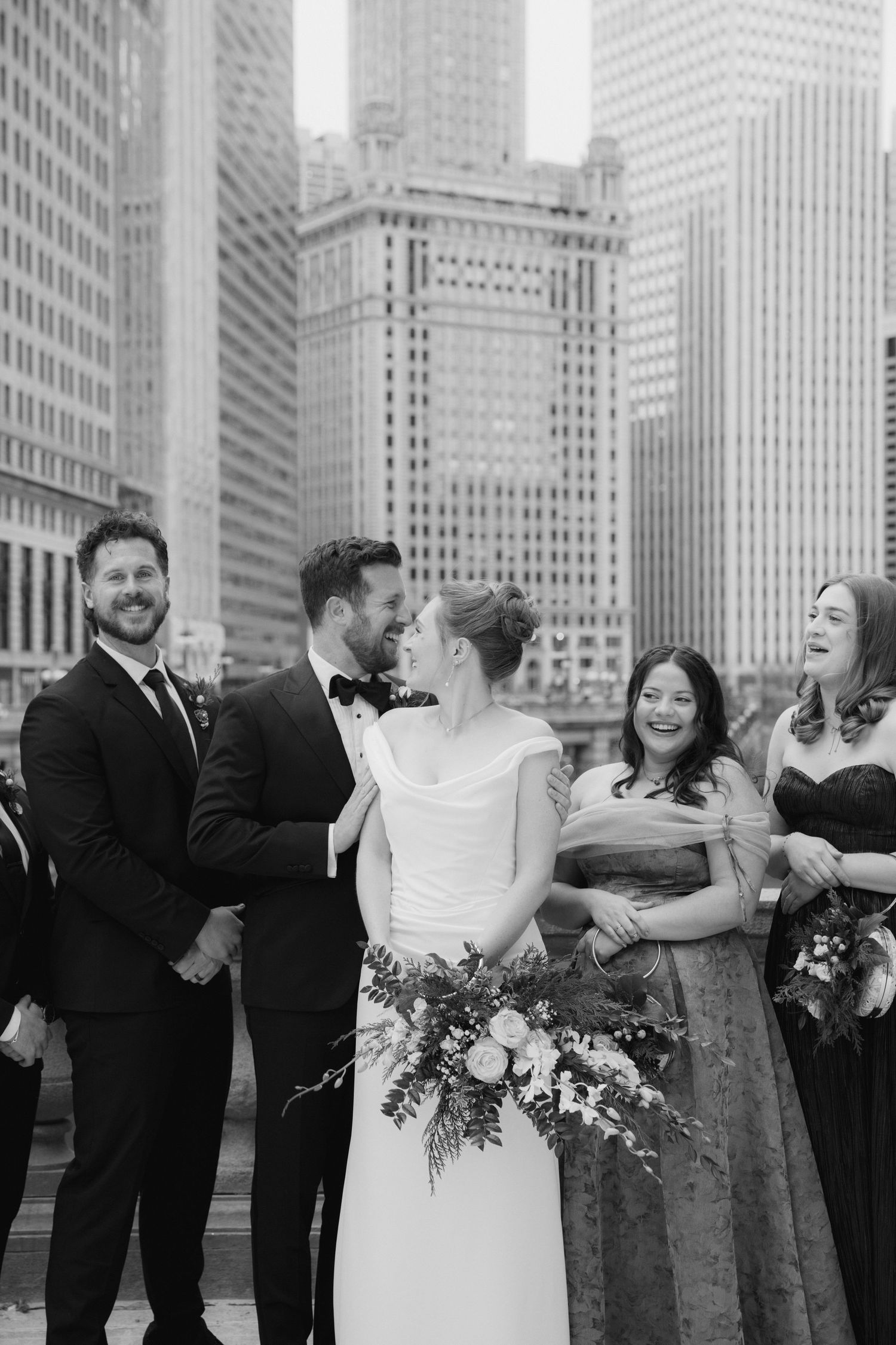 Wedding party sharing a joyful moment against backdrop of urban skyscrapers in black and white.