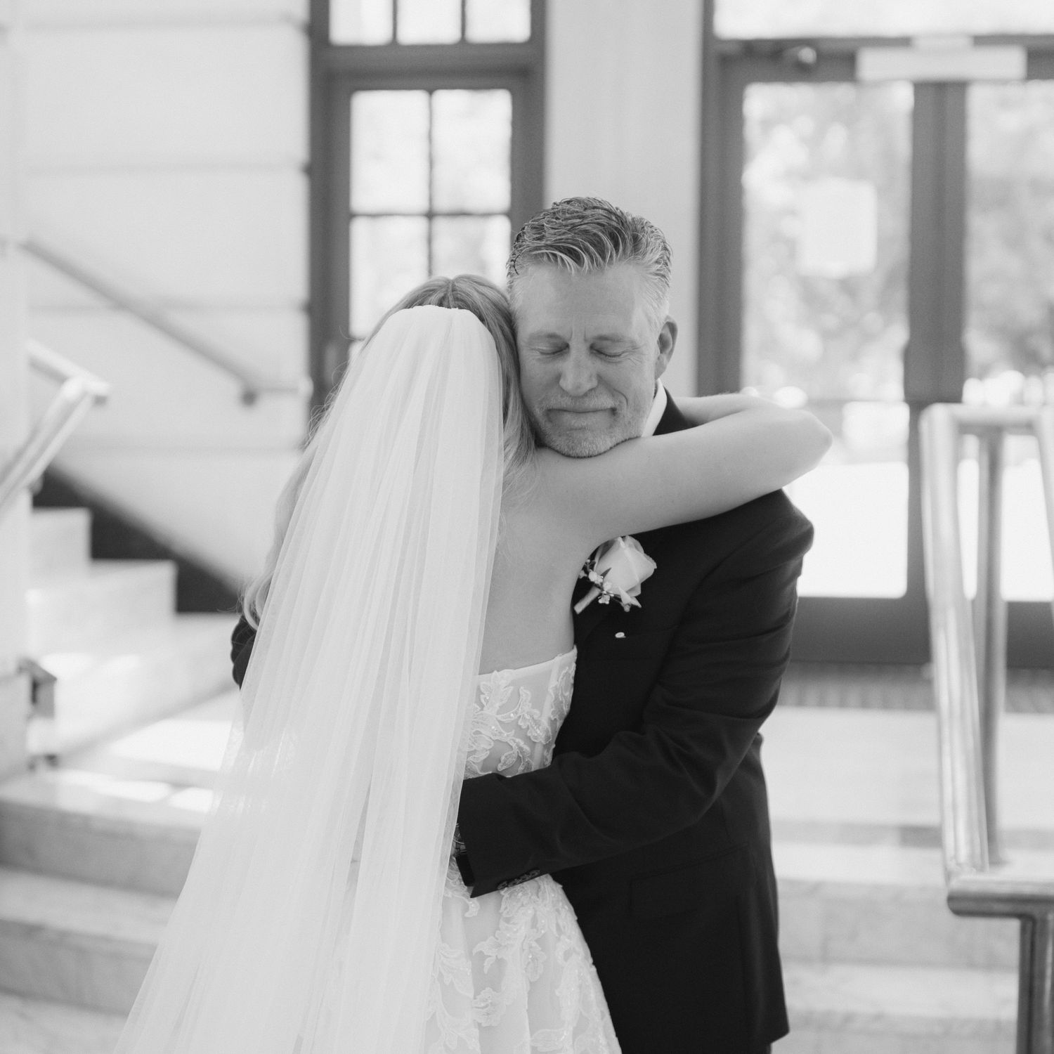 A tender embrace between newlyweds in black and white, with the bride's flowing veil and groom in classic tuxedo.