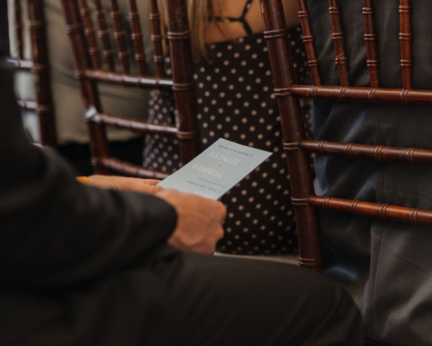 Person reading on a Kindle e-reader while seated next to wooden furniture in a dimly lit room.