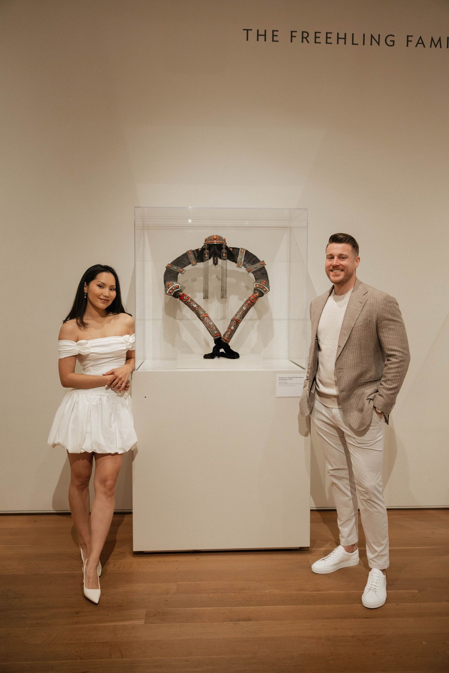 Engaged couple posing together in art museum wearing white dress and beige suit.