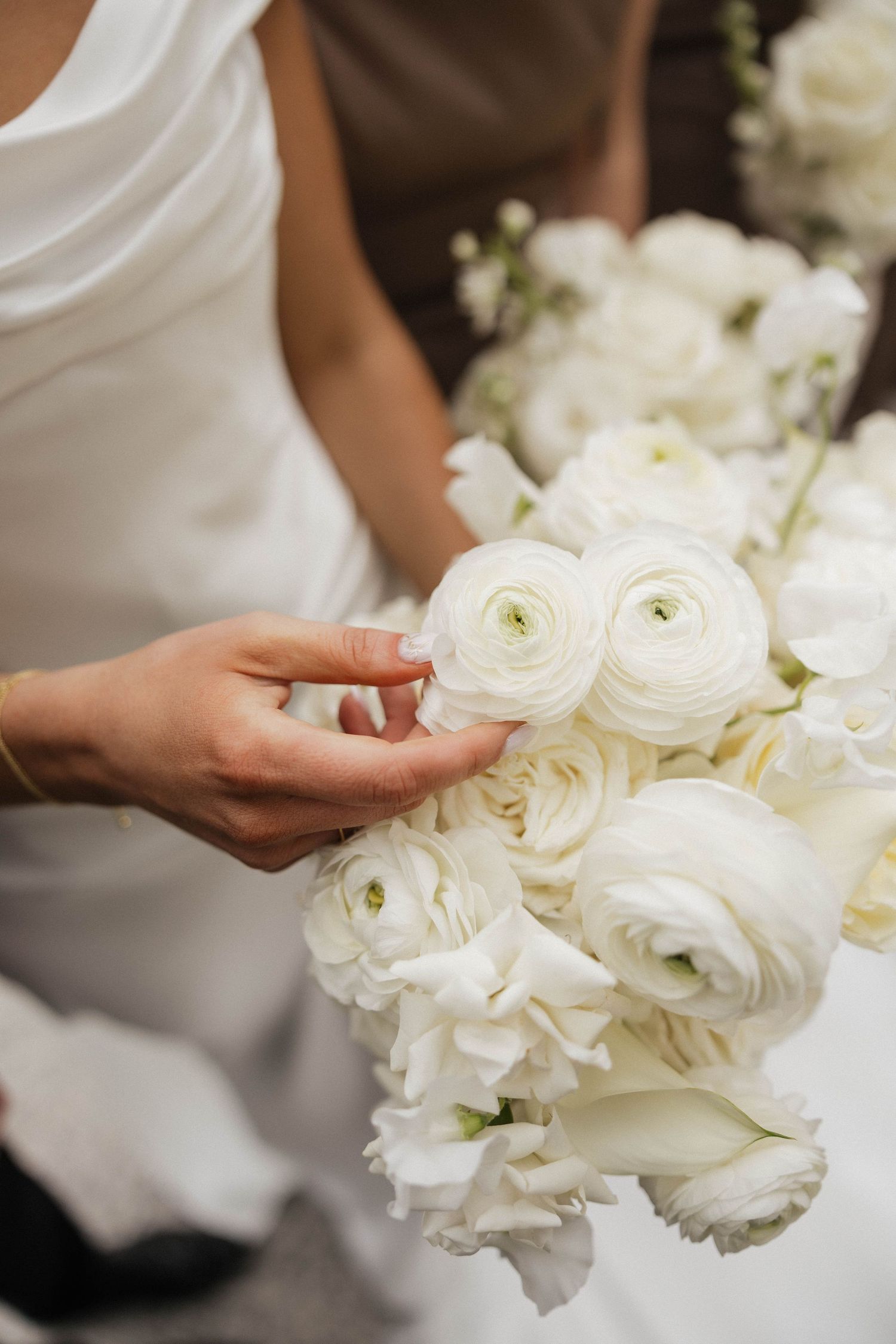 Bride holding elegant white ranunculus and rose wedding bouquet in close-up detail.