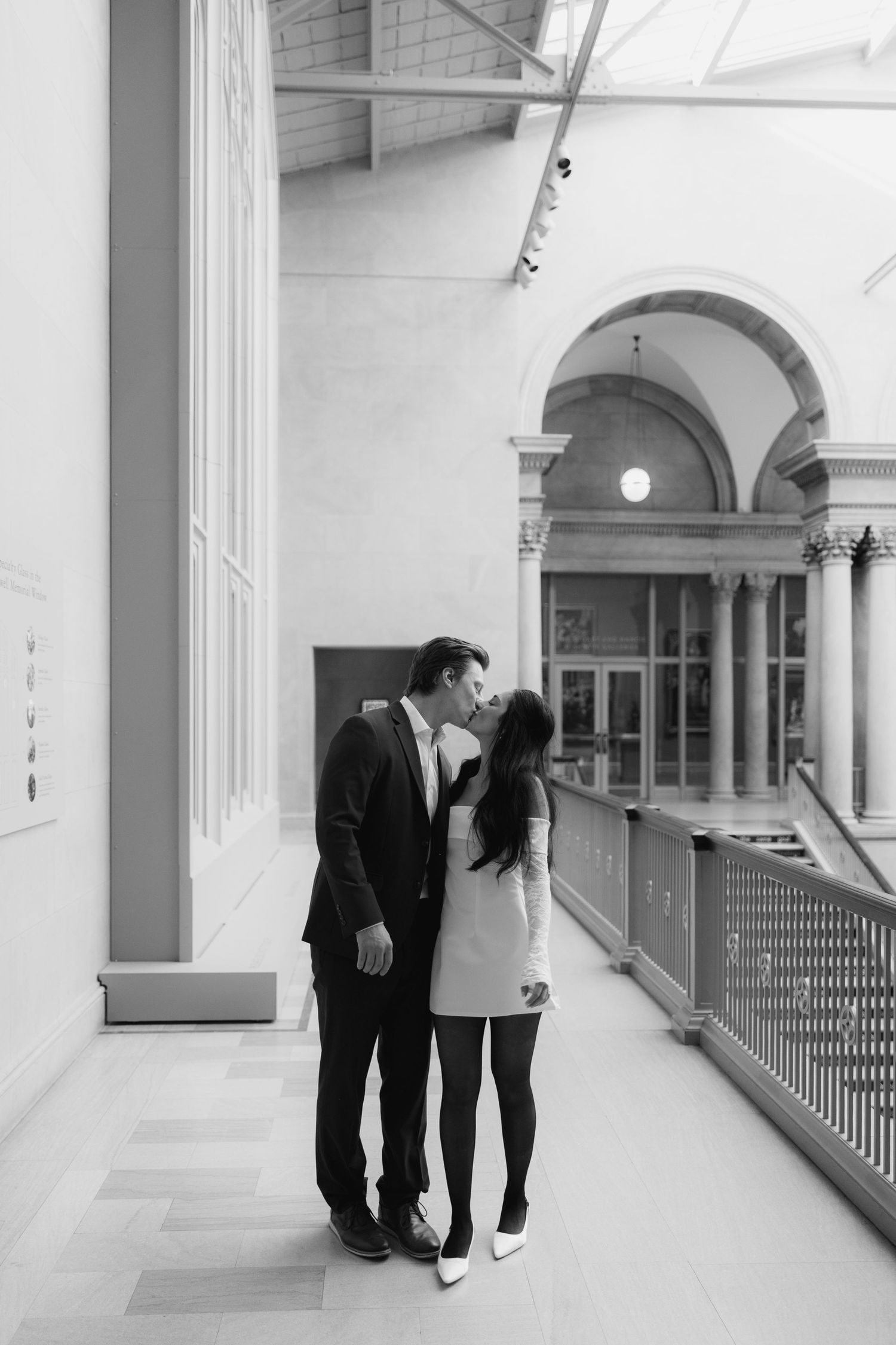 Black and white photo of couple walking through classical columned hallway.