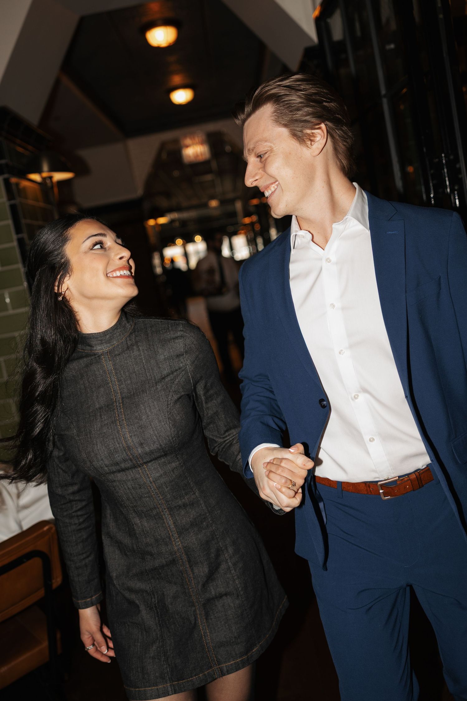 A couple shares a romantic moment in a dimly lit restaurant setting with warm lighting.