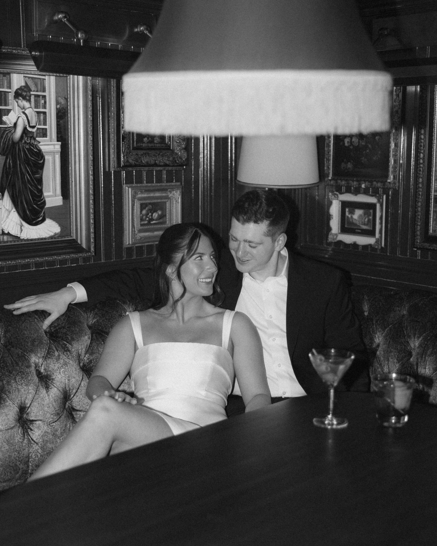 A black and white photograph showing people seated at a bar or lounge under lamp lighting.