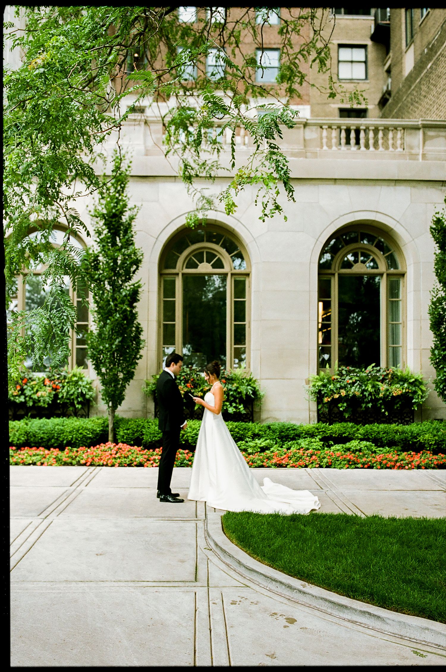 Bride and groom share first look moment in elegant courtyard garden outside a grand stone building.