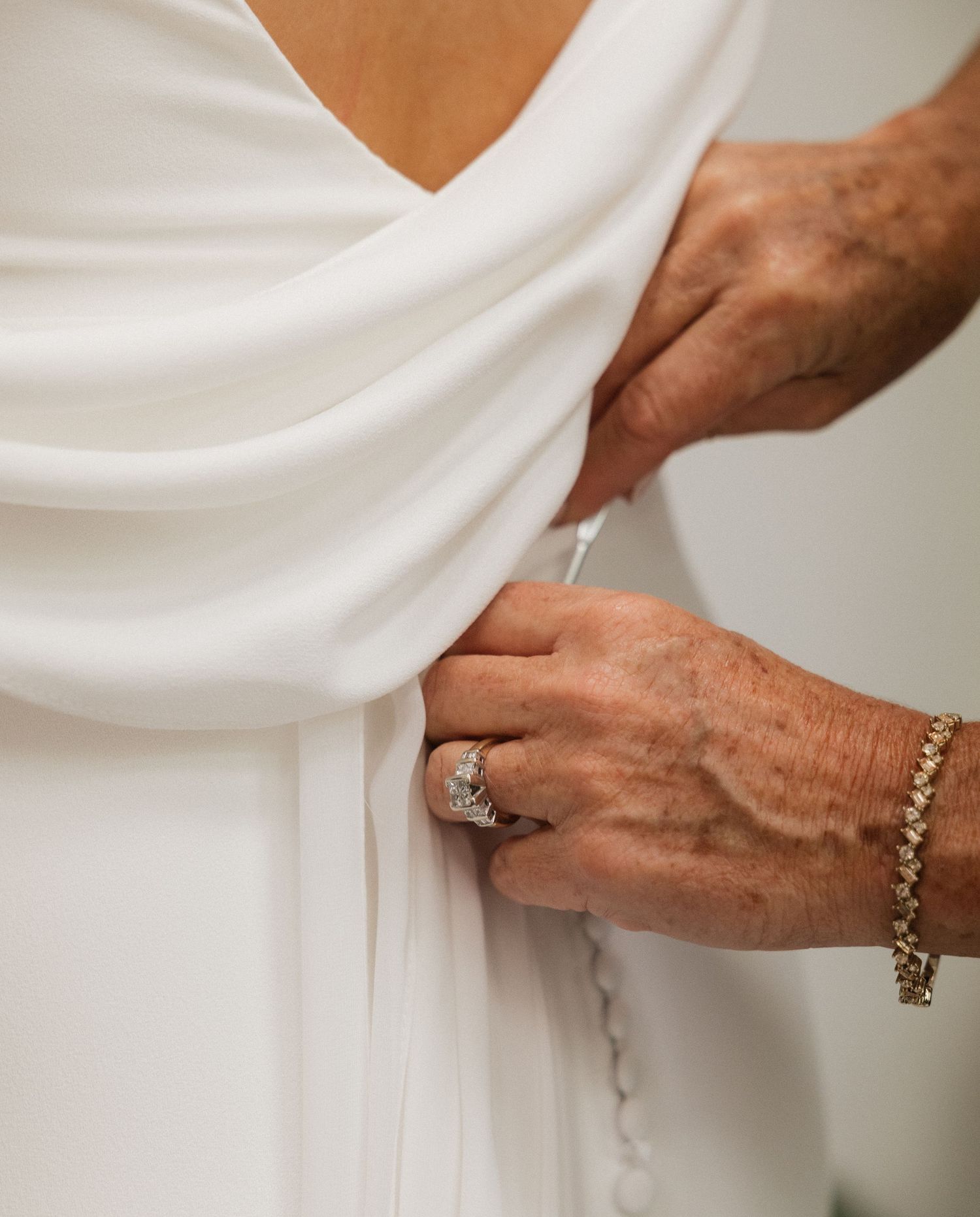 Close-up view of hands adjusting a white wedding dress with delicate details and jewelry.