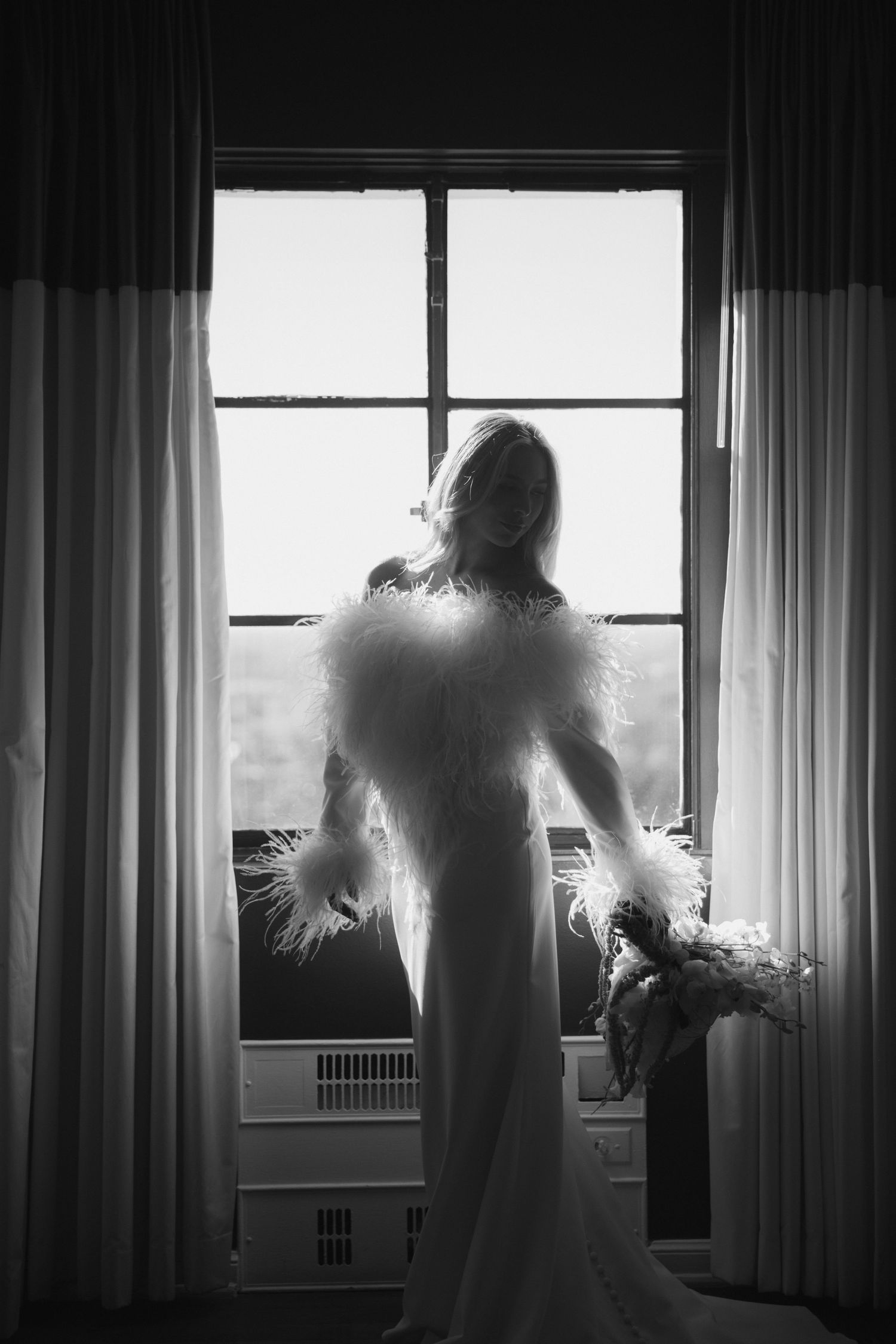 A silhouetted figure stands by a bright window in a moody black and white photo series.