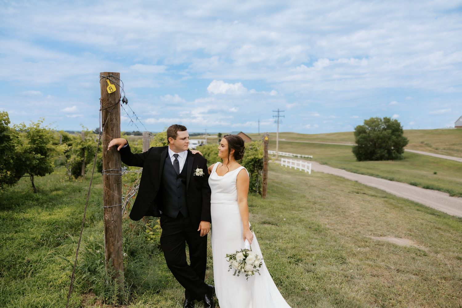 Newlyweds share romantic moments in an open field under blue skies.