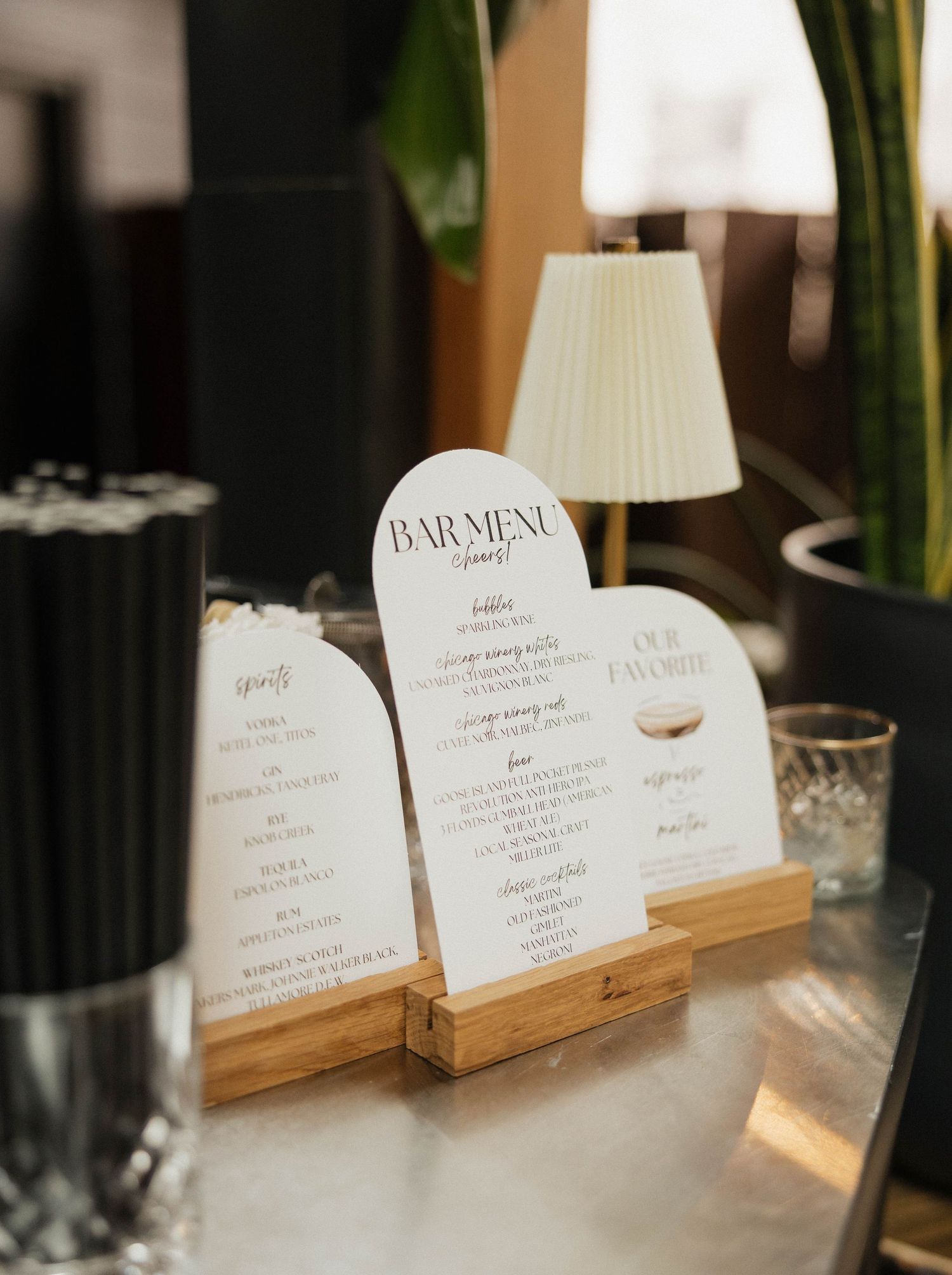 Elegant arch-shaped wedding bar menu displayed on wooden stand at modern reception venue.