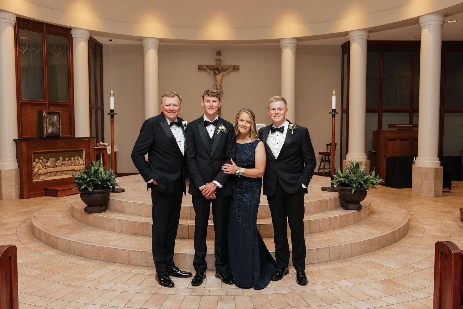 Family of four posing in formal attire inside a church with a crucifix backdrop.