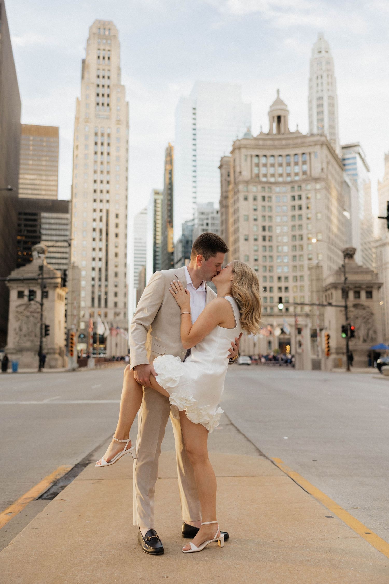 Couple kissing on a city street with Chicago skyscrapers in the background at sunset.