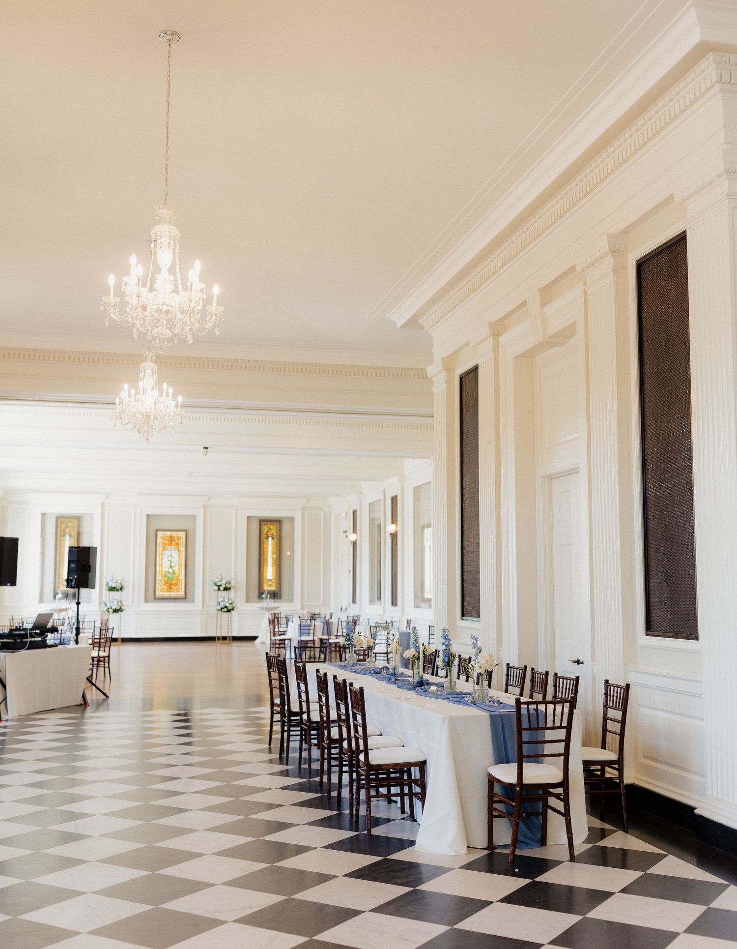 Elegant ballroom with black and white checkered floor, white walls, and crystal chandeliers in a historic building.
