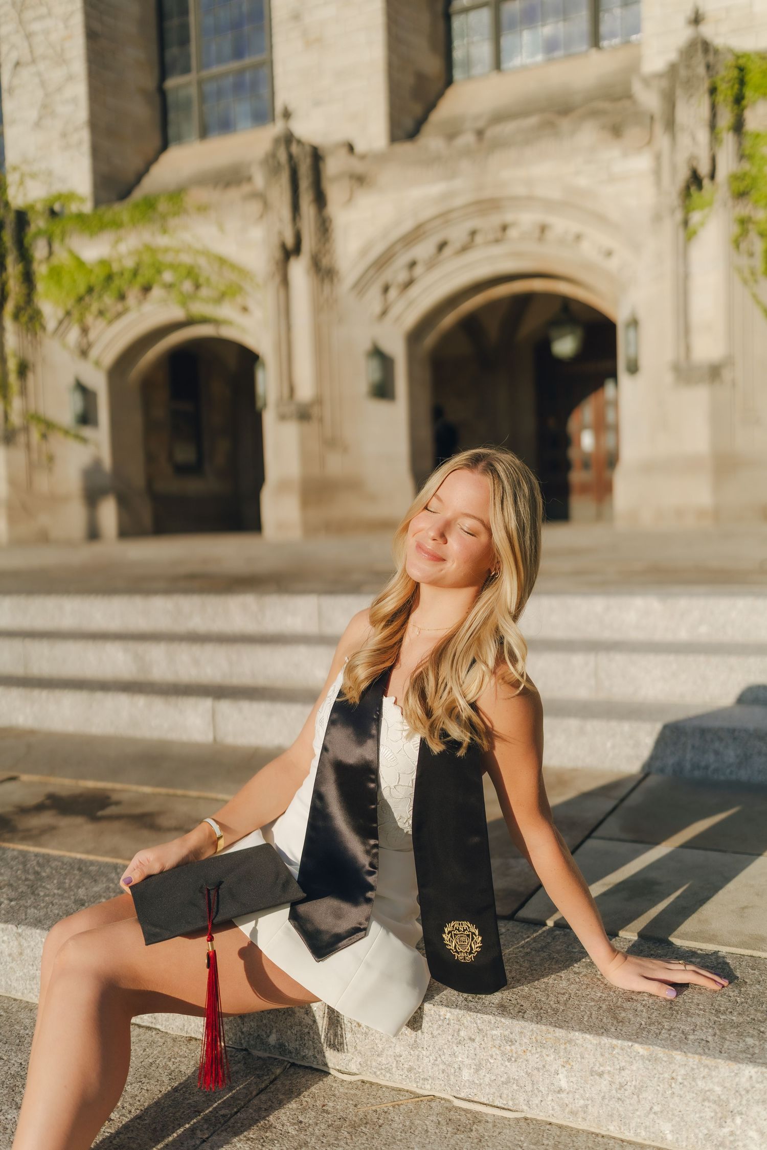 A woman in a black blazer and shorts poses dramatically on stone steps in an architectural setting.
