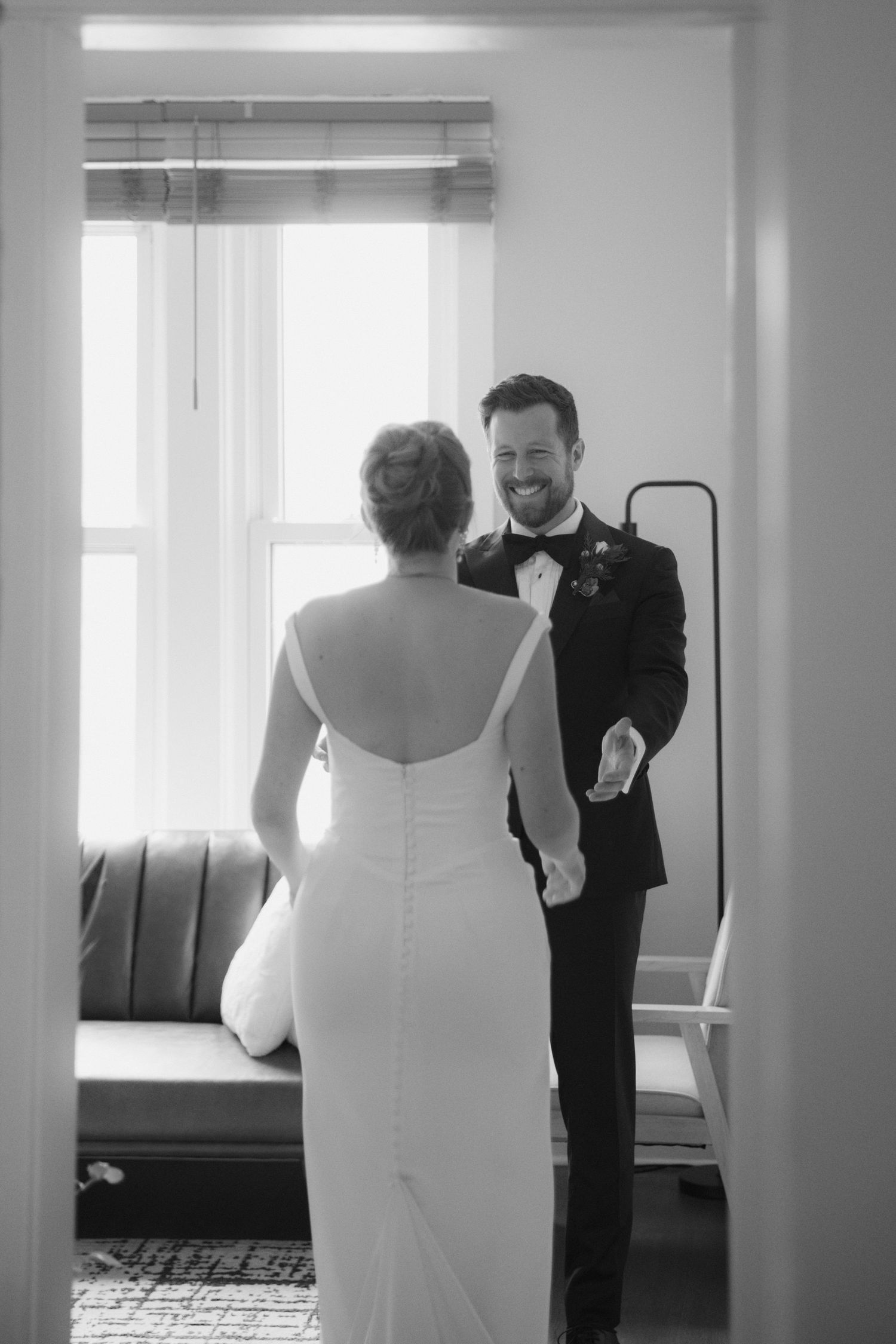 Black and white series showing a wedding first look moment as a bride in white dress reveals herself to a waiting groom.
