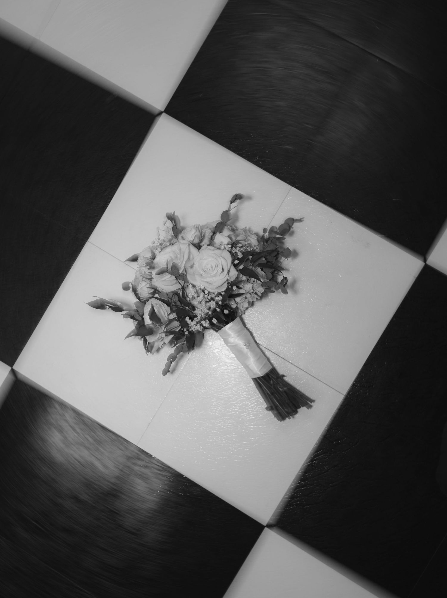 Black and white photo of floral arrangements on a checkered surface creating an artistic composition.