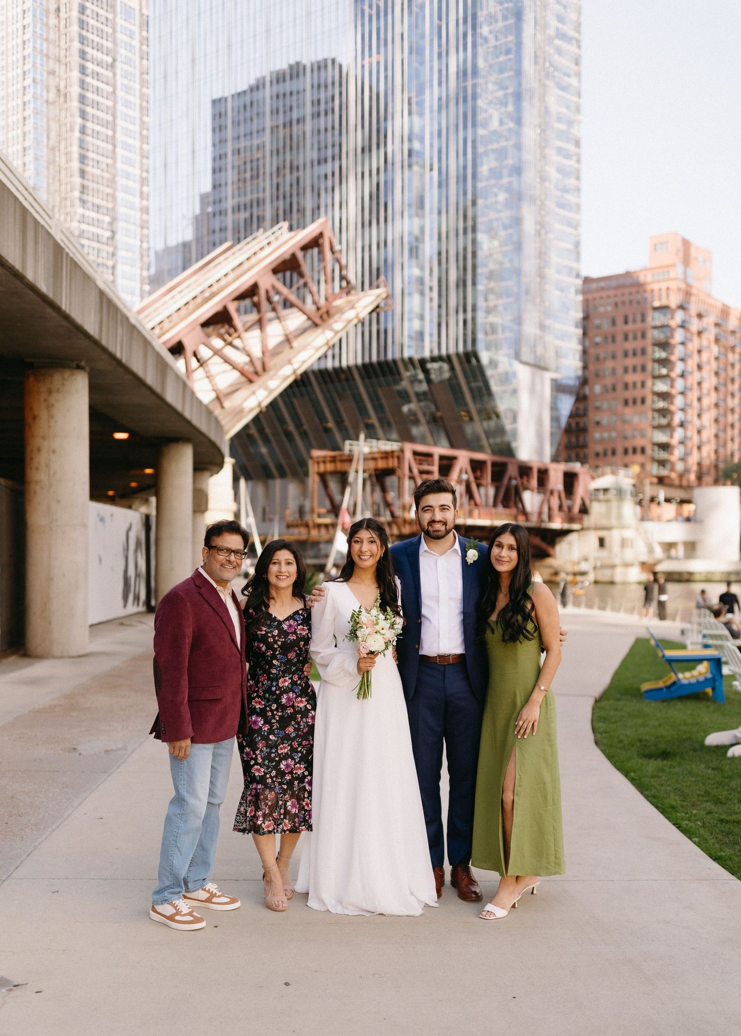 A group poses together under a concrete architectural structure in an urban setting with tall buildings in the background.