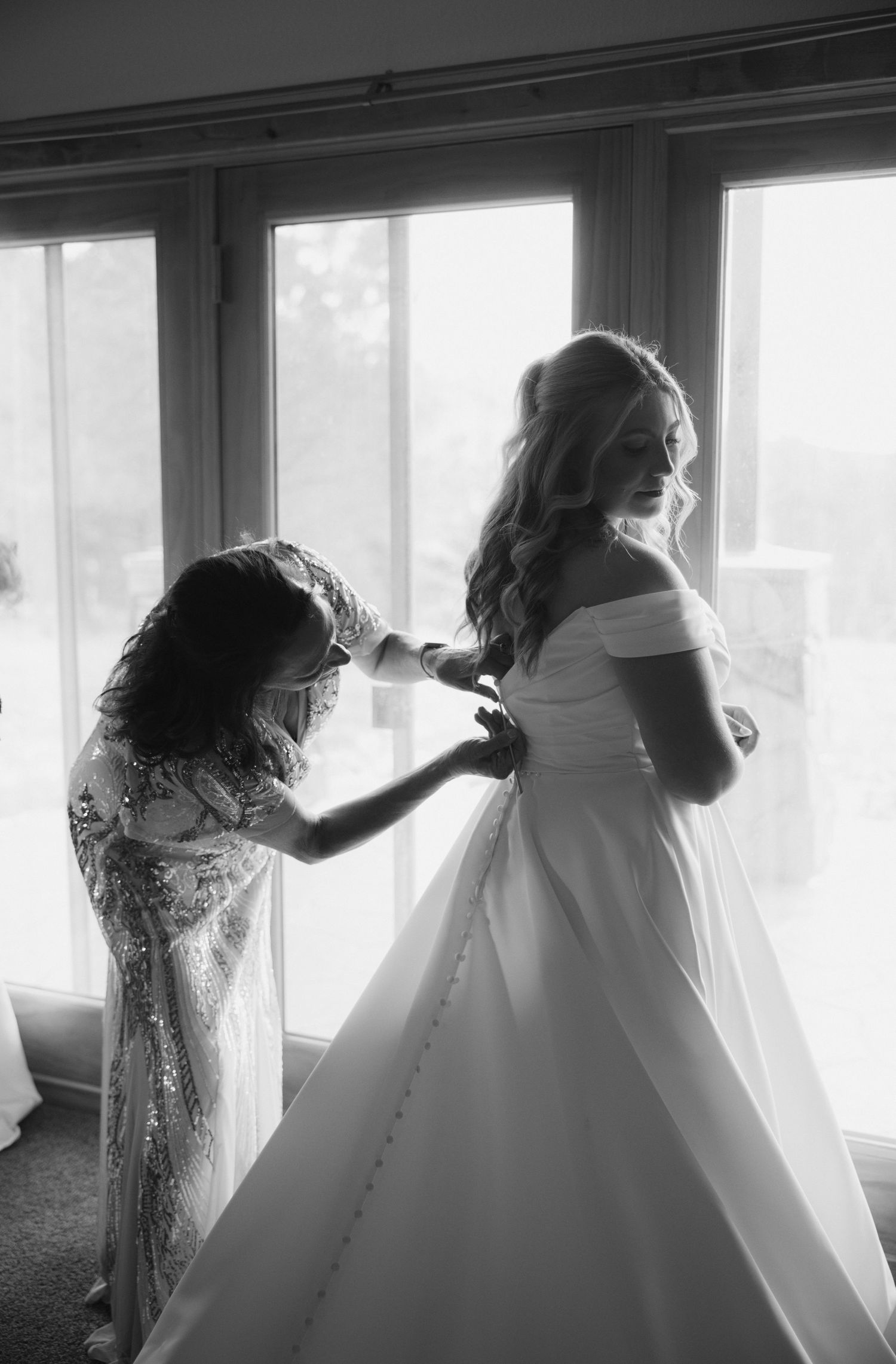 Wedding dress being adjusted in a sunlit room with large windows.
