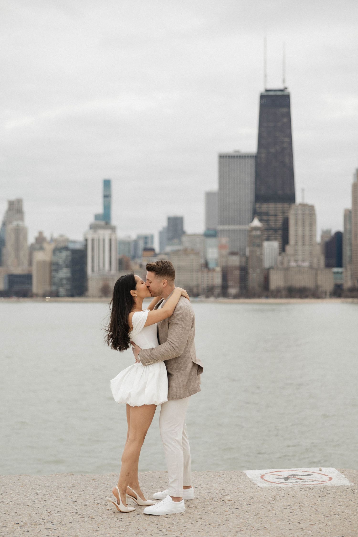 Couple kissing on Chicago lakefront pier with John Hancock Tower skyline backdrop.
