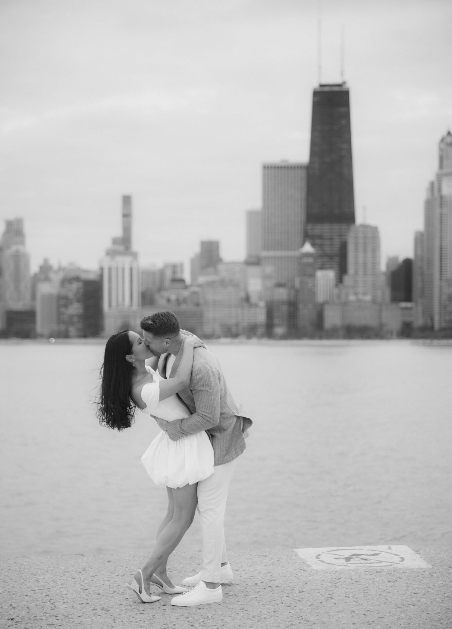 Black and white photo of couple kissing near Chicago skyline by the lakefront.