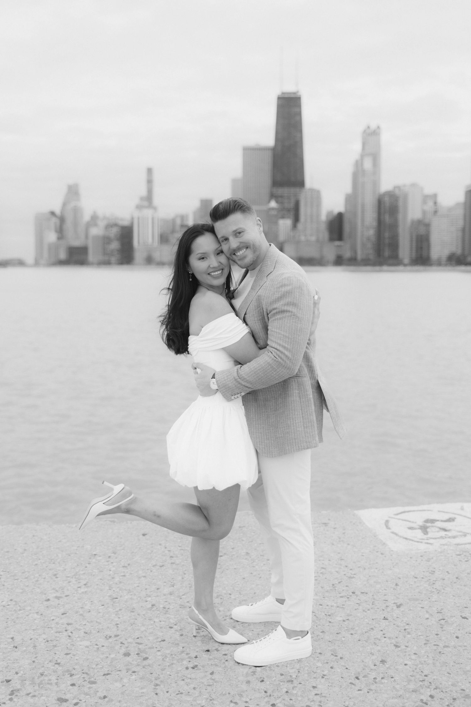 Black and white photo of a couple embracing and smiling with the Chicago skyline in the background.