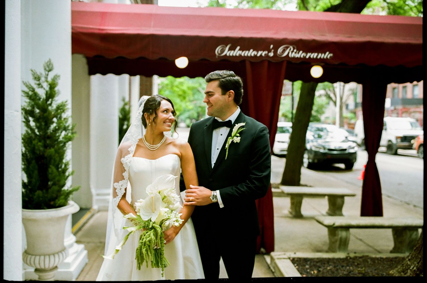 Bride and groom smiling outside Salvatore's Ristorante, bride holding white bouquet in elegant wedding attire.