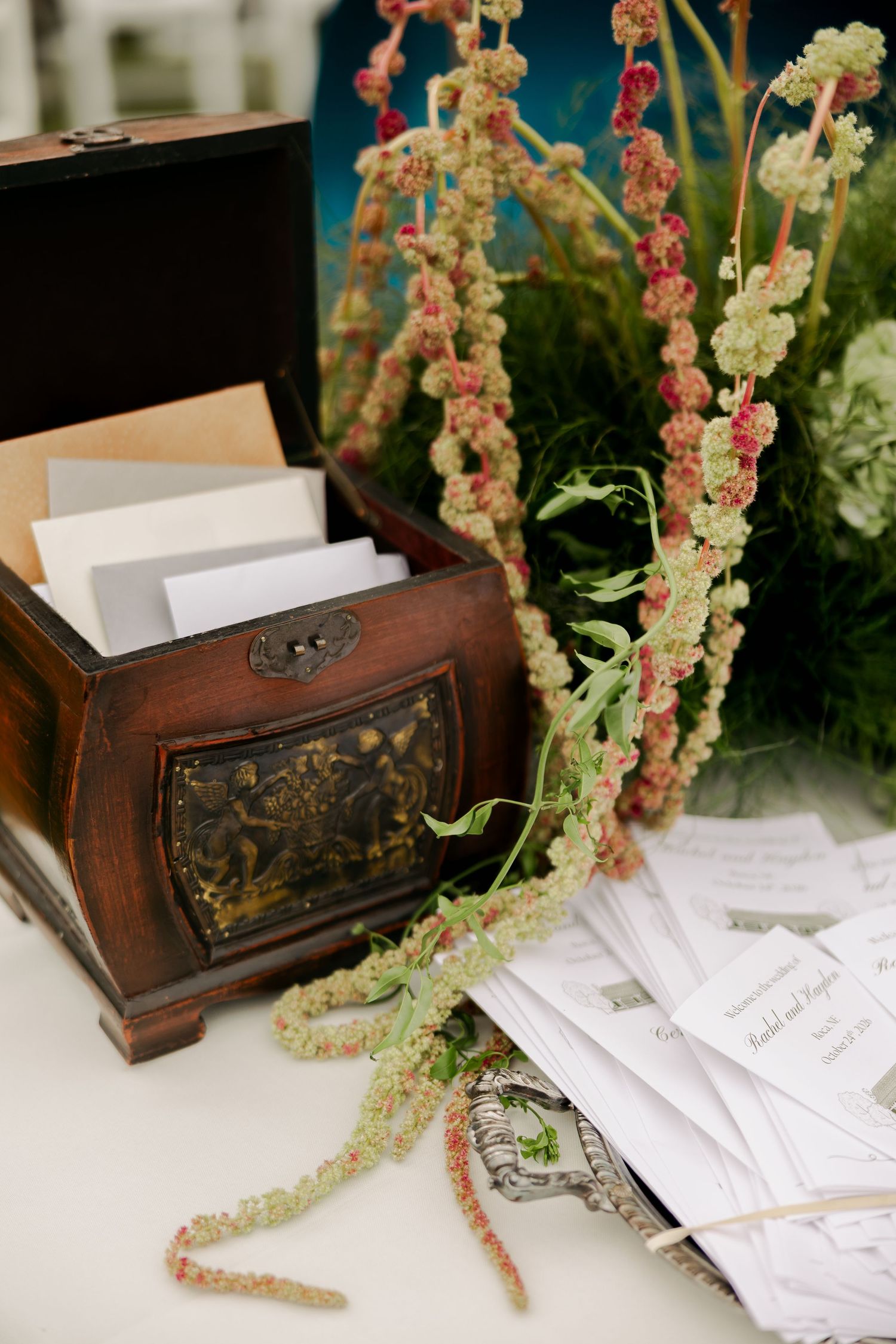 Rustic wooden card box with guest envelopes and place cards on a table decorated with trailing green and pink amaranth.